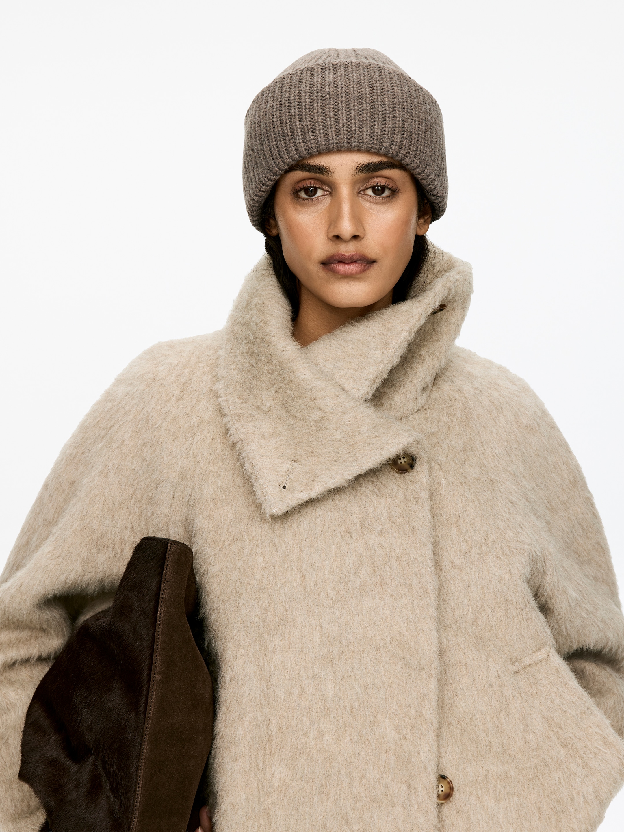 View larger image: A taupe double-fold wool beanie, knitted in a half cardigan stitch, is being worn by the model, covering her head.