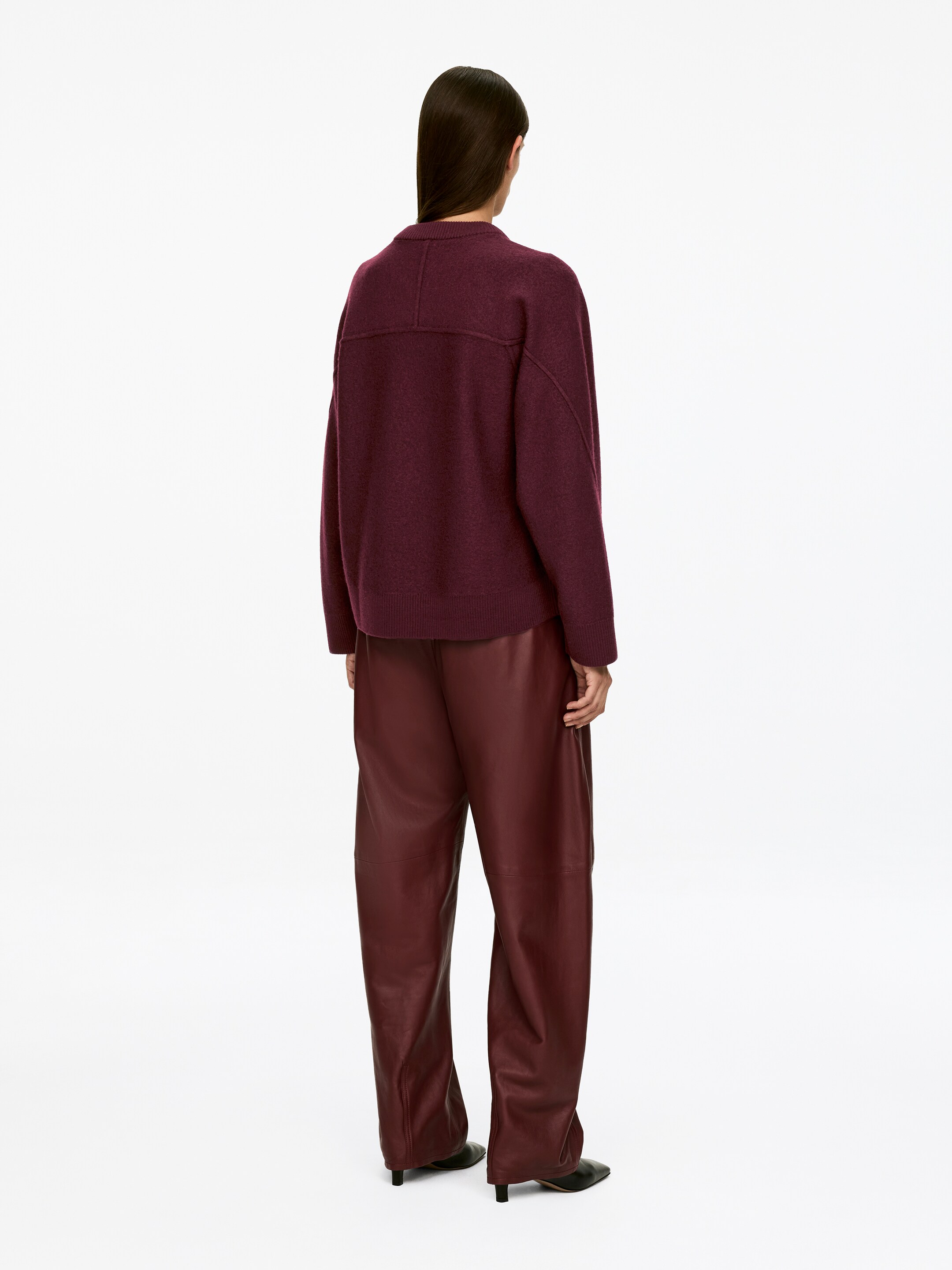 Agrandir l'image: Un cardigan en laine bouillie d'un rouge profond, avec une coupe ample, un ourlet côtelé et des détails de couture distincts sur le haut du dos, est porté par le mannequin. Le mannequin porte également un pantalon rouge profond assorti.