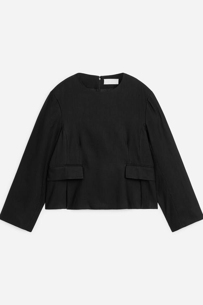 A black long-sleeved top is shown from the front, featuring a round neckline, wide long sleeves, and a cropped hem. The structured top features two flap pockets at the lower front and a short zip detail at the back of the collar. - 1