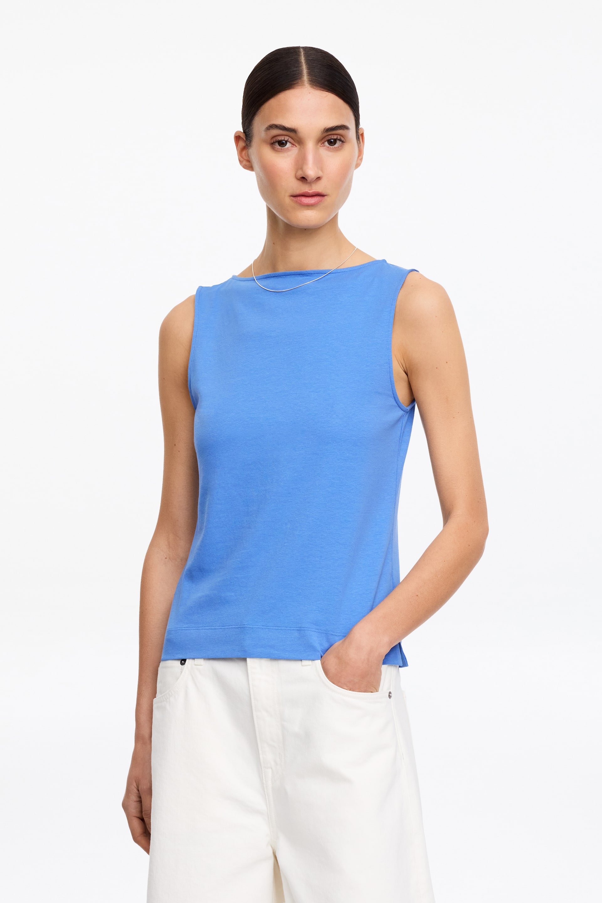 Visa större bild: En blå åtsittande linne med båtringning och slitsar vid sidosömmarna bärs av modellen, som också har på sig ett silverhalsband.