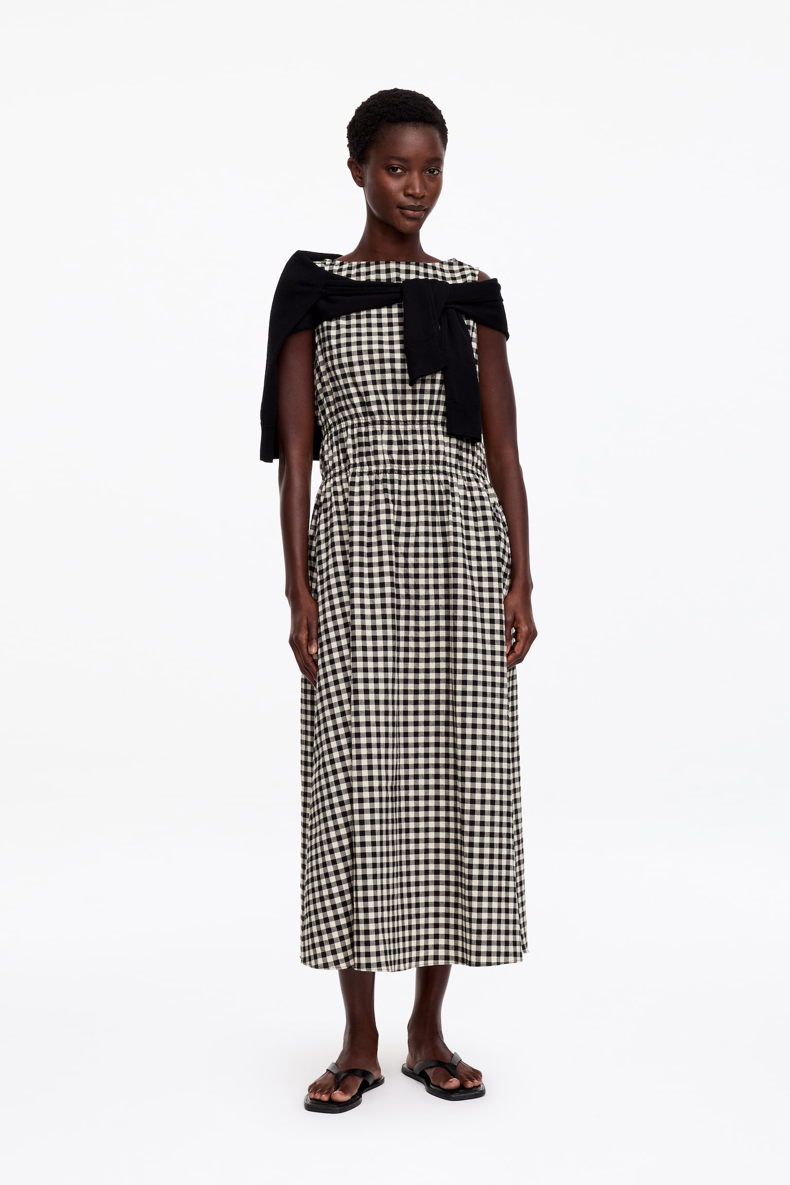 Um vestido midi sem mangas é apresentado de frente, com um padrão xadrez preto e branco e um decote barco. Um franzido suave define a cintura, a partir da qual a saia flui até ao comprimento do tornozelo, exibindo uma textura subtil de seersucker. - 1