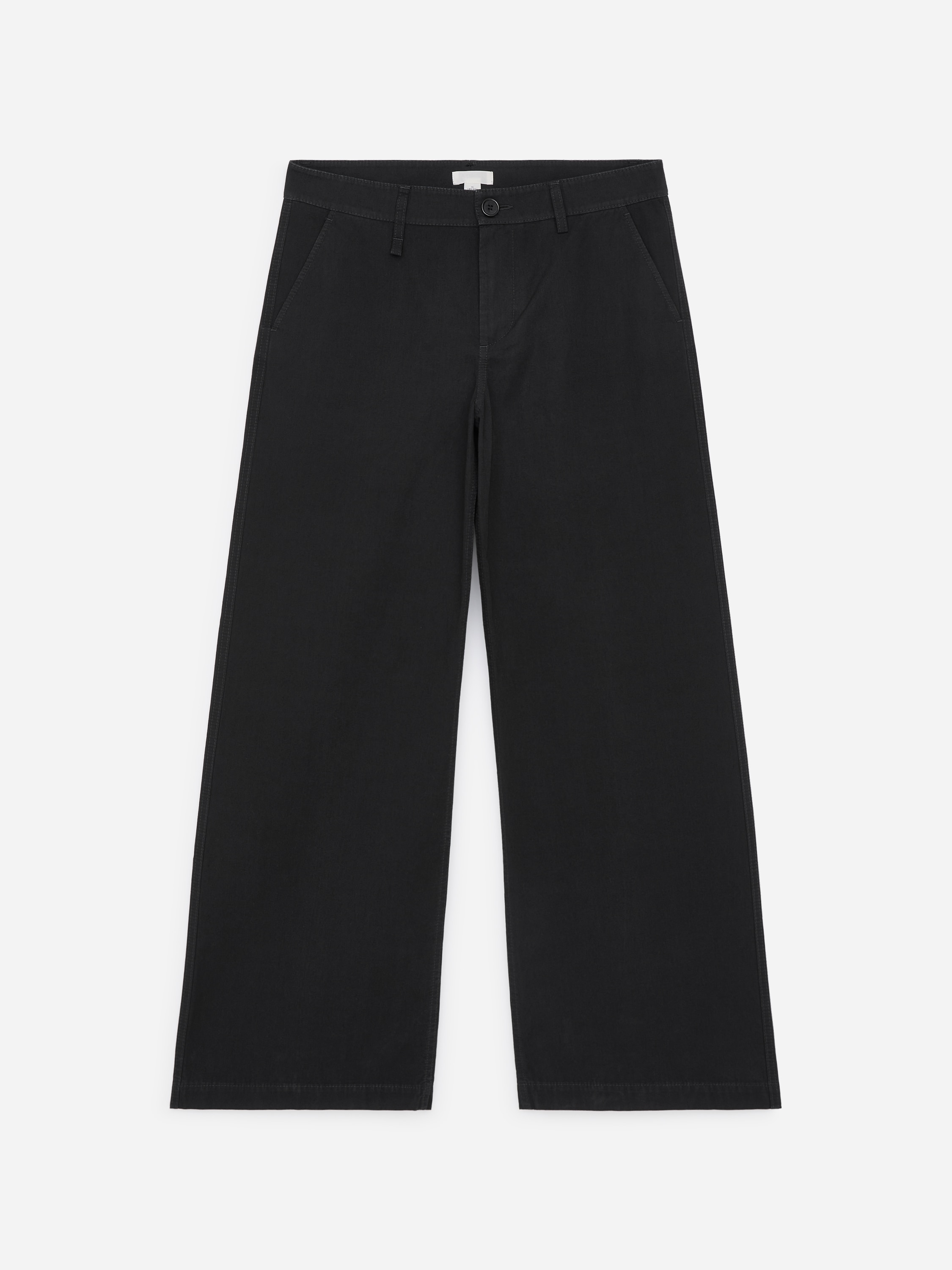 Il modello indossa pantaloni chino neri a gamba larga, con una mano appoggiata nella tasca laterale. I pantaloni sono abbinati a una cintura in pelle nera, a un maglione scollato a V grigio scuro sovrapposto a una T-shirt bianca e a sandali neri.