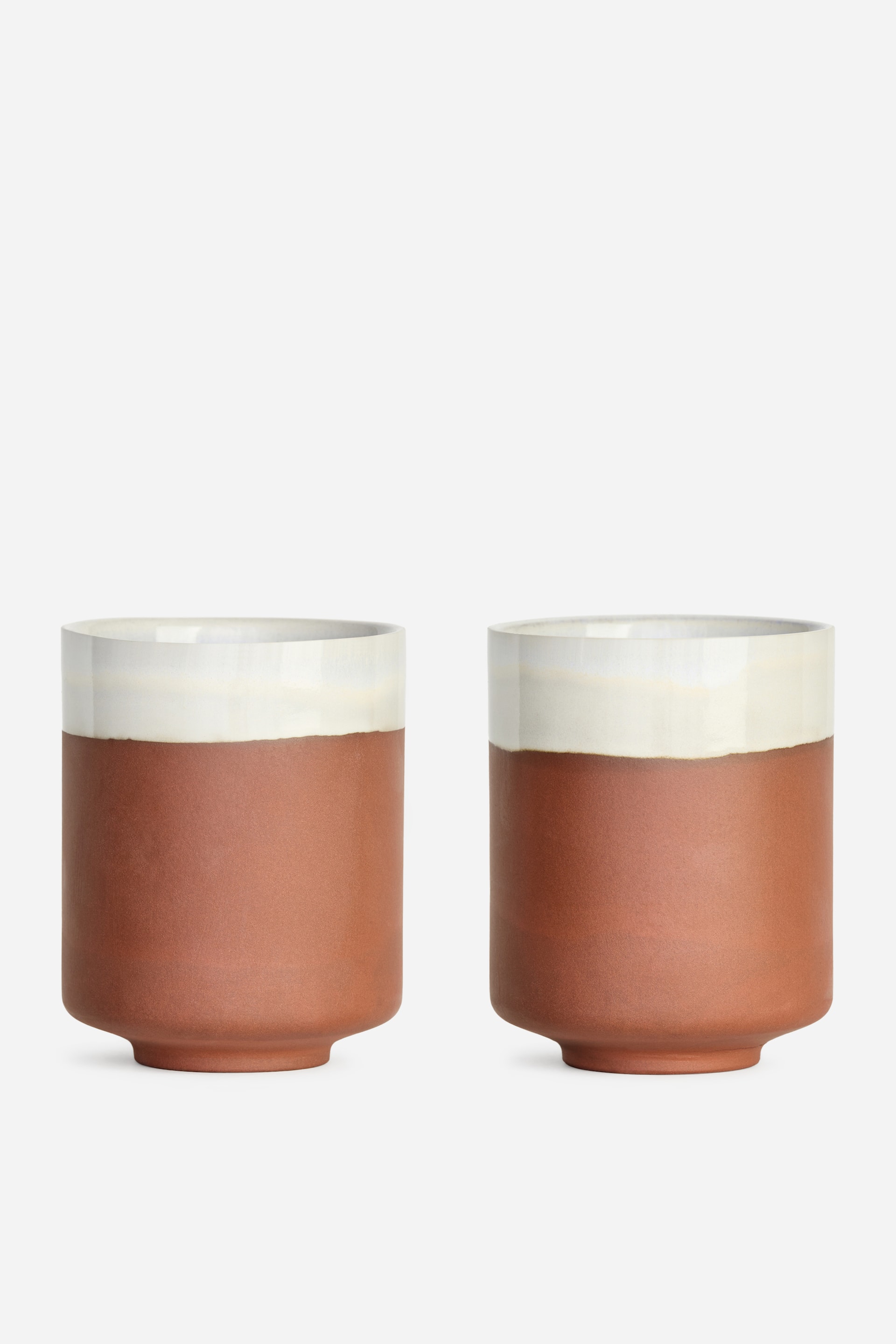 Ver imagen más grande: Un par de tazas cilíndricas se encuentra de frente, cada una con una sección inferior mate de color marrón rojizo y un borde superior blanco marfil brillante, con una base sutilmente acampanada.