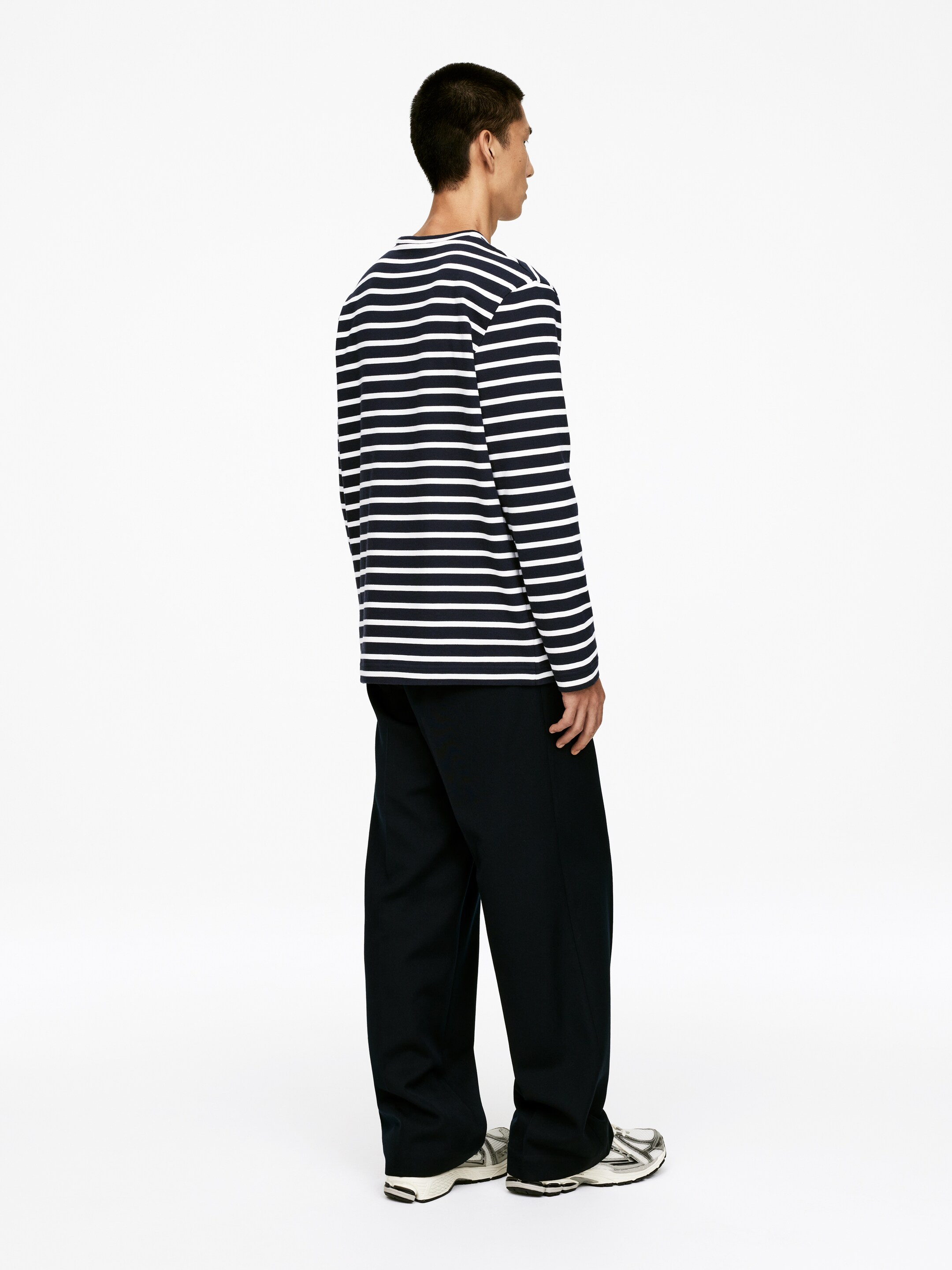 Grotere afbeelding bekijken: Een shirt met lange mouwen en een ronde hals, met horizontale marineblauwe en witte strepen, wordt gedragen. Het shirt heeft een ontspannen pasvorm en wordt gestyled met donkere, wijde broekspijpen, gezien vanuit een rechter profiel.