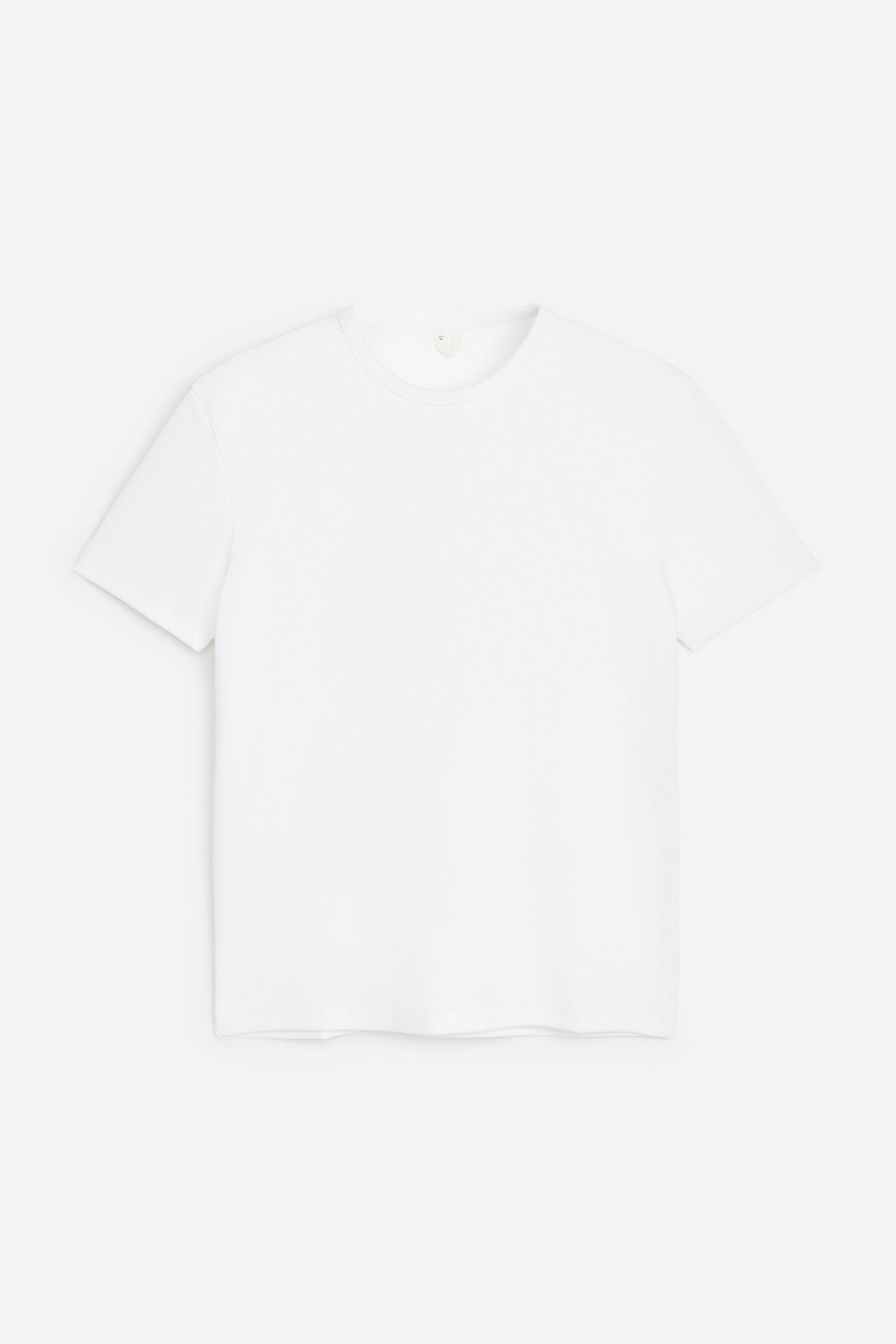 Agrandir l'image: Un t-shirt blanc à manches courtes est posé à plat, face avant visible. Il présente un col rond avec une bande côtelée étroite et un ourlet droit, avec une petite étiquette de couleur claire visible à l’intérieur de la bande du col à l’arrière.