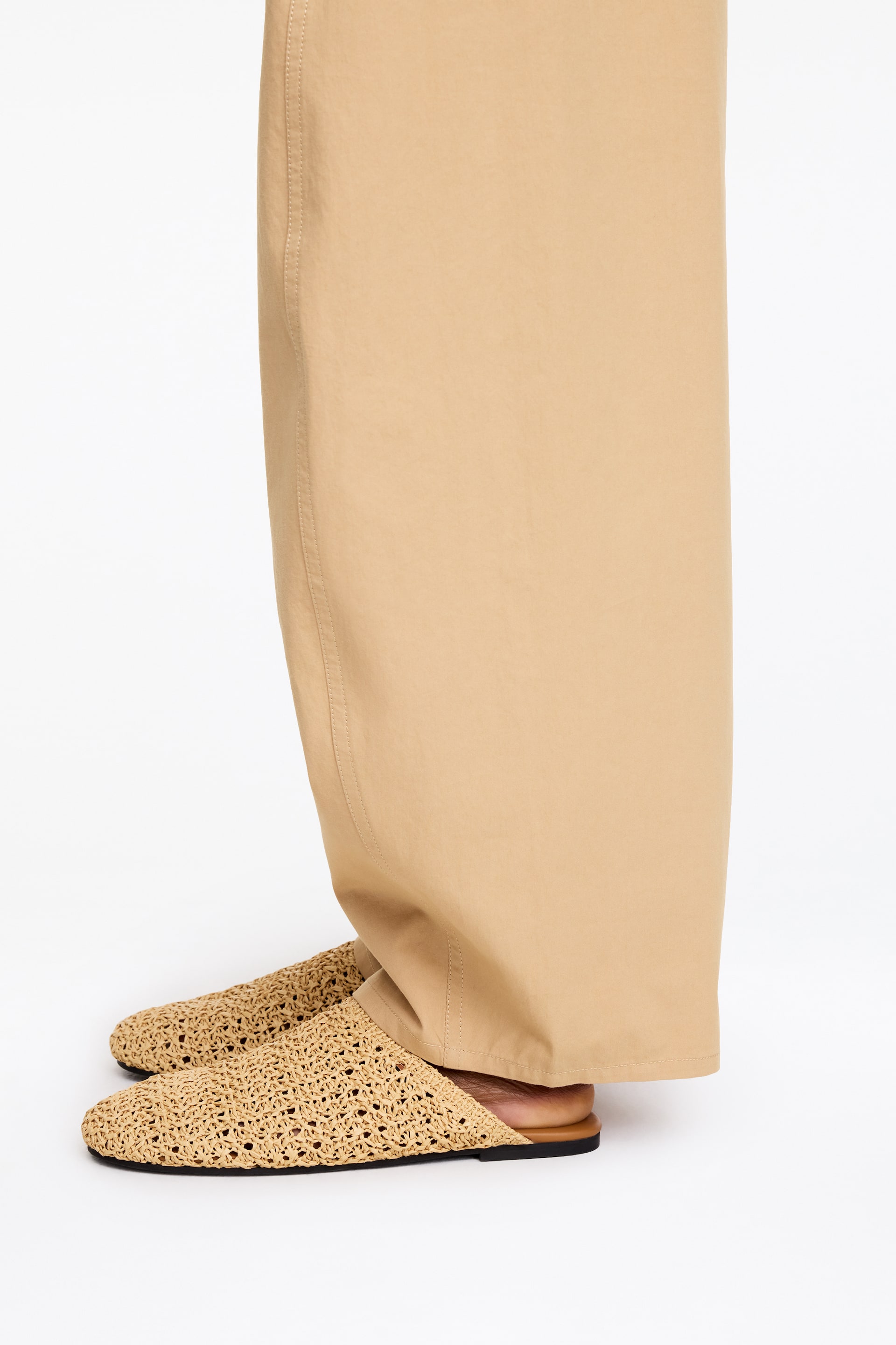 View larger image: Light brown crocheted mule slippers are worn by the model. The slippers feature a rounded toe and a thin dark outsole, styled with wide-leg beige trousers.