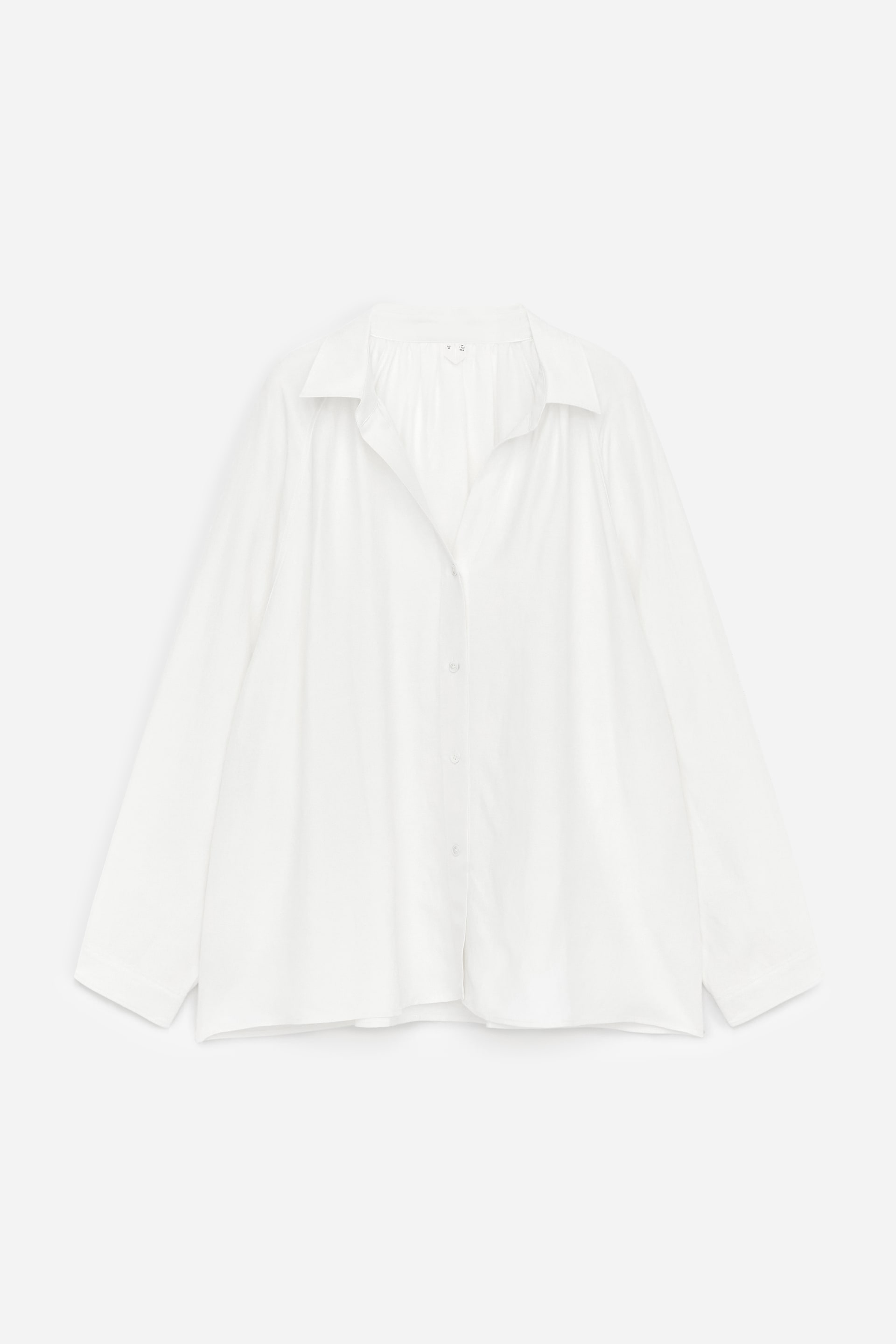 Agrandir l'image: Une chemise blanche présente sa vue de face, avec une coupe volumineuse et un froncement au niveau de l'encolure. Le tissu tombe doucement, affichant un col décontracté, une patte de boutonnage complète avec des boutons blancs, et des manches longues.