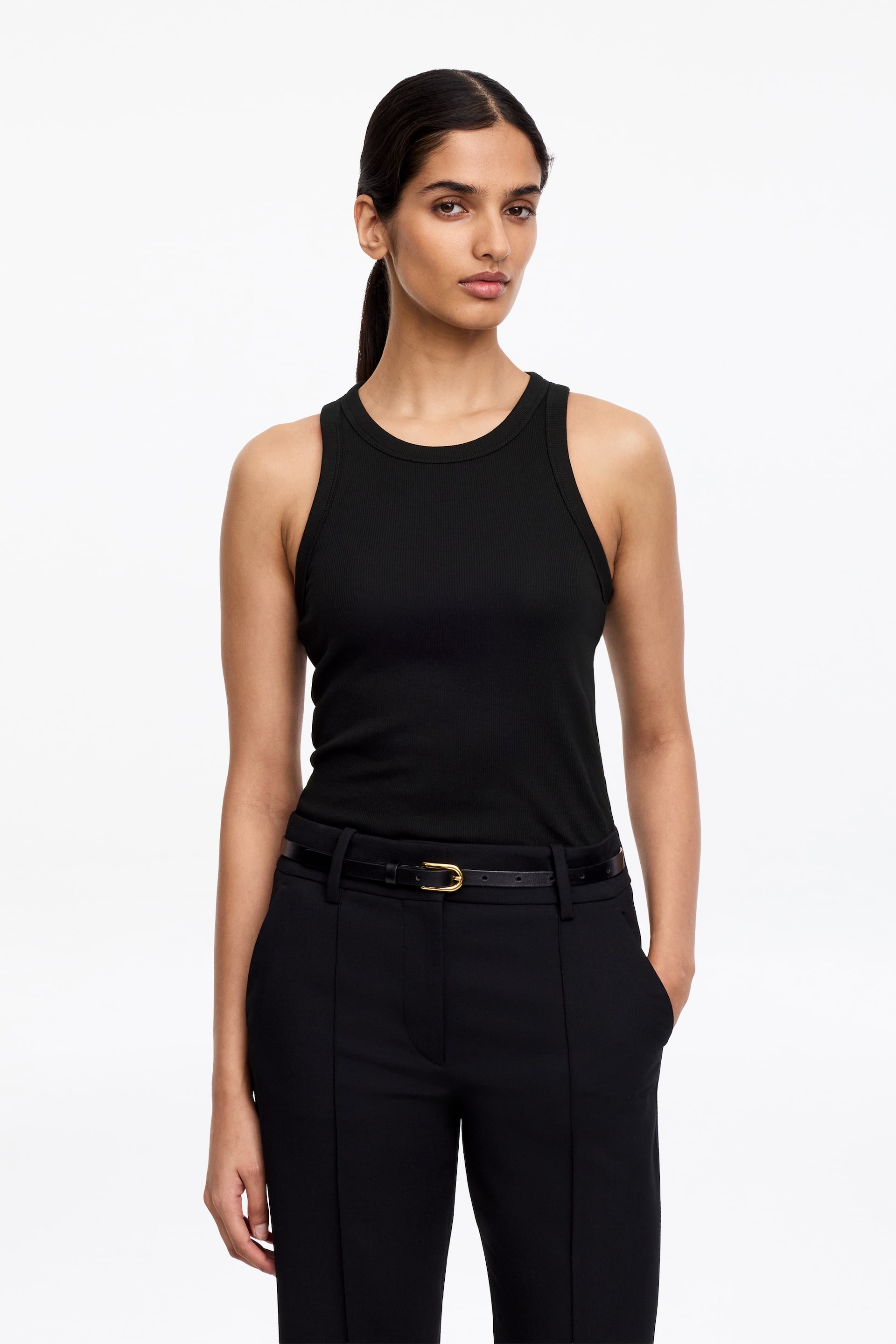 Agrandir l'image: Un débardeur noir côtelé est porté, avec un col rond, des bretelles épaisses et une silhouette ajustée, rentré dans un pantalon noir.