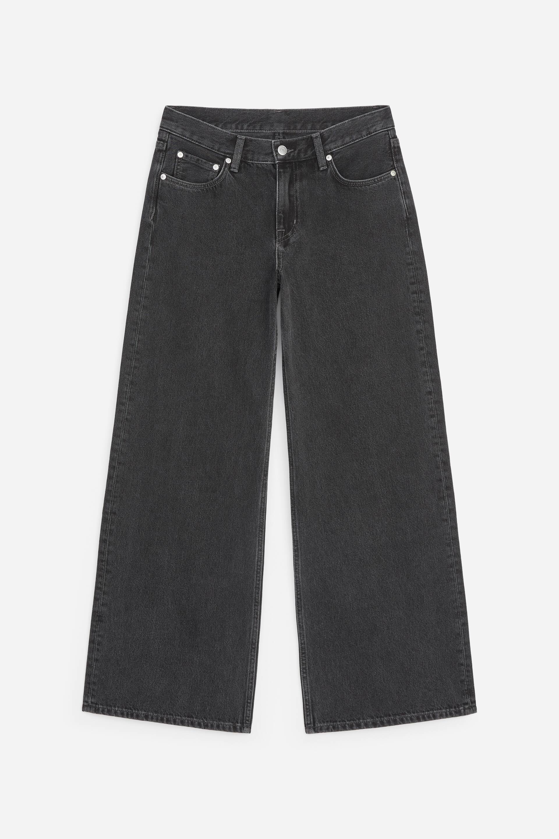 Grotere afbeelding bekijken: Donkergrijze jeans met wijde pijpen worden van voren getoond. Ze zijn voorzien van een knoop- en ritssluiting, riemlussen, twee voorzakken en een muntzakje, allemaal geaccentueerd met zilverkleurige metalen klinknagels. De pijpen zijn wijd en recht gesneden tot aan de zoom.
