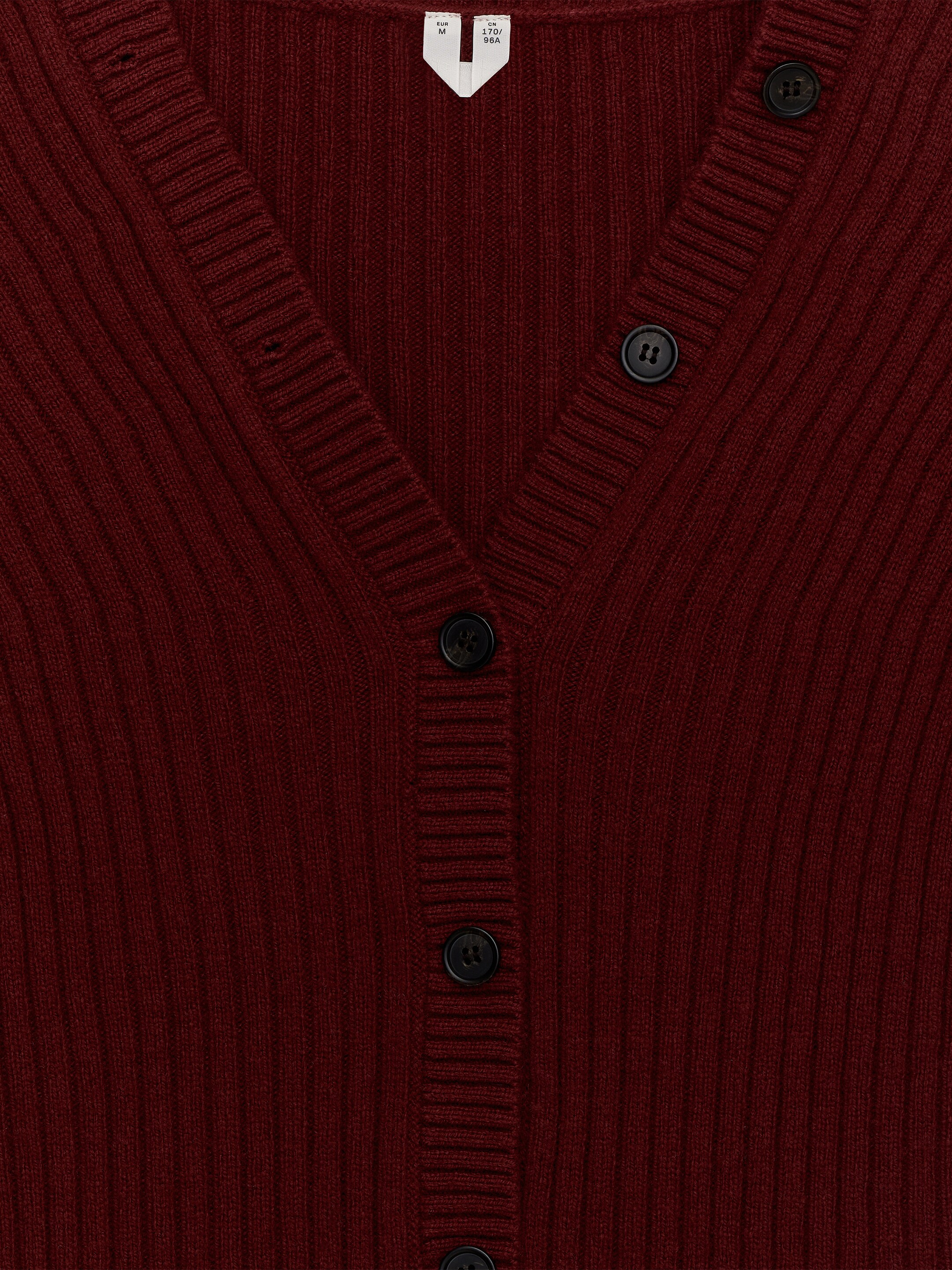 Agrandir l'image: L'AVANT d'un cardigan tricoté côtelé en rouge foncé est exposé, avec un col en V côtelé et une patte de boutonnage centrale allongée ornée de boutons ronds foncés.