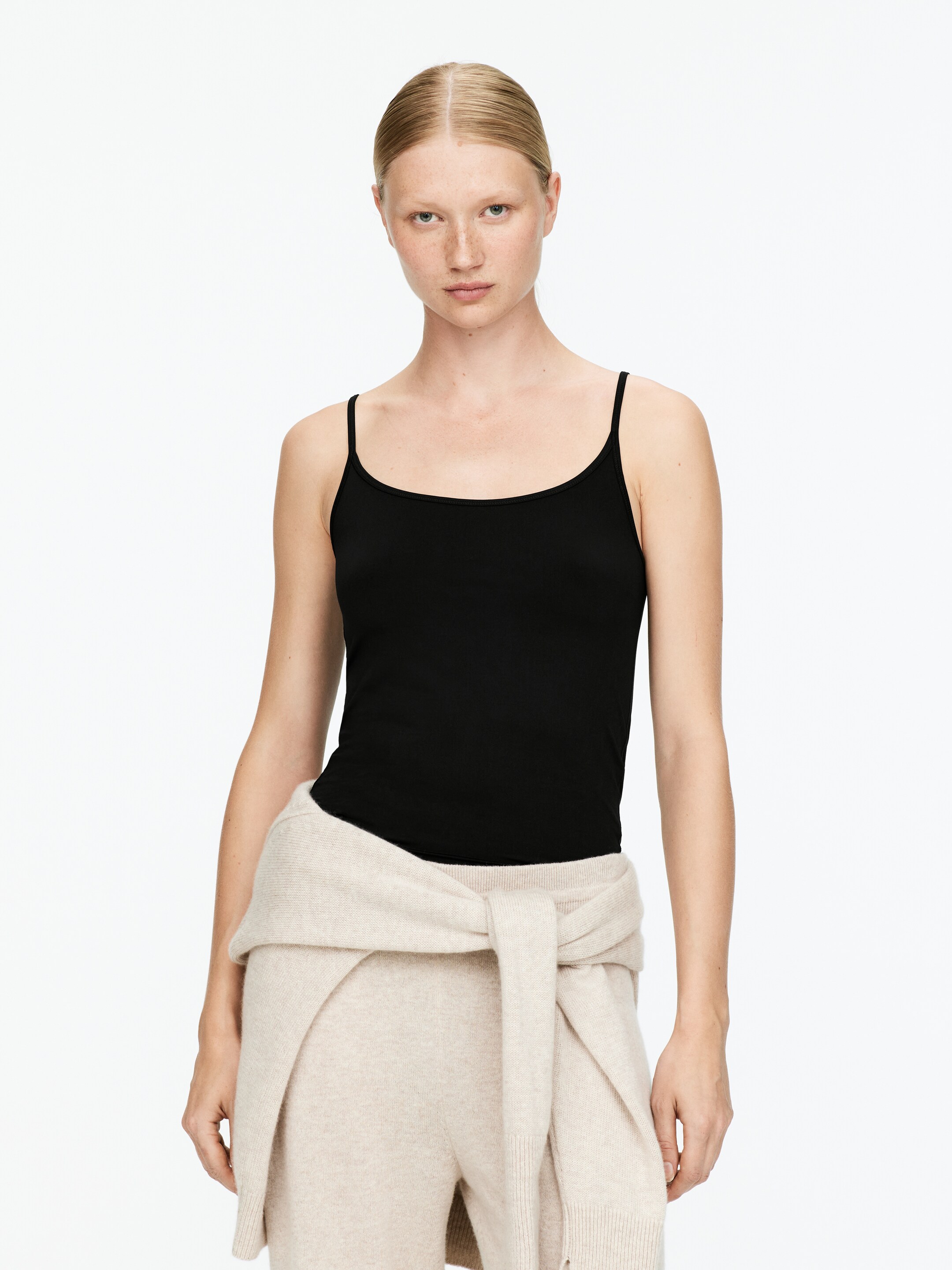 Grotere afbeelding bekijken: Een zwarte camisole top wordt aan de voorkant gepresenteerd, met dunne spaghettibandjes en een ondiepe ronde halslijn. De top sluit nauw aan op het lichaam en toont zijn gladde textuur en slanke silhouet.