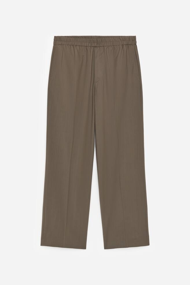 The brownish-green trousers are shown from the front, showcasing an elasticated, gathered waistband. Side seam pockets are visible, and the wide-leg trousers present straight legs with subtle vertical creases. - 1