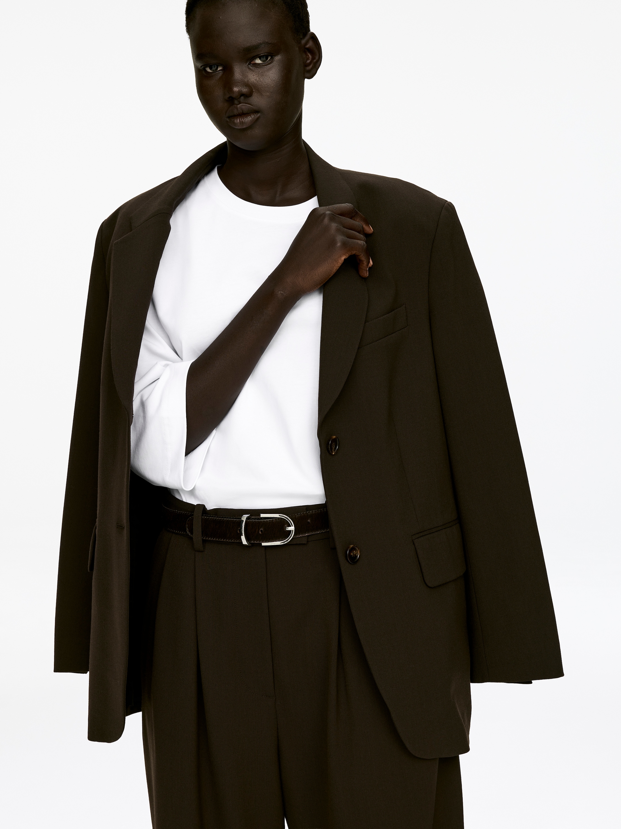 Agrandir l'image: Un T-shirt blanc à col rond, confectionné en jersey de coton épais et nettement structuré avec des manches 3/4, est porté par le mannequin. Le T-shirt est superposé sous un blazer sombre et est rentré dans un pantalon foncé.