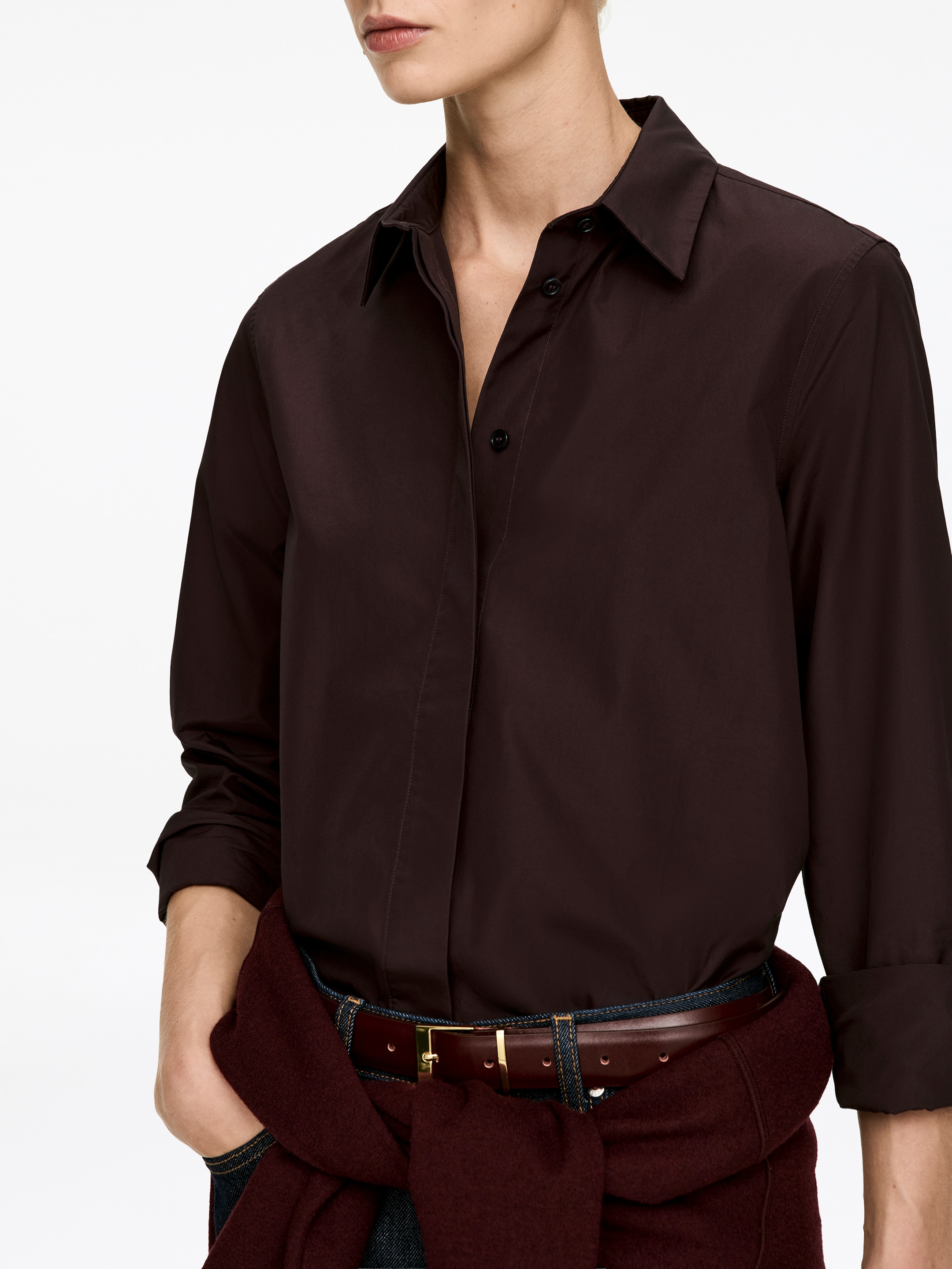 Ingrandisci l'immagine: Una camicia marrone scuro con bottoni è indossata, caratterizzata da un colletto a punta parzialmente sbottonato e una cannoncino frontale visibile con bottoni scuri. Le sue maniche lunghe sono arrotolate ai polsini, e la camicia presenta una vestibilità rilassata, drappeggiando liberamente dalle spalle alla linea della vita.