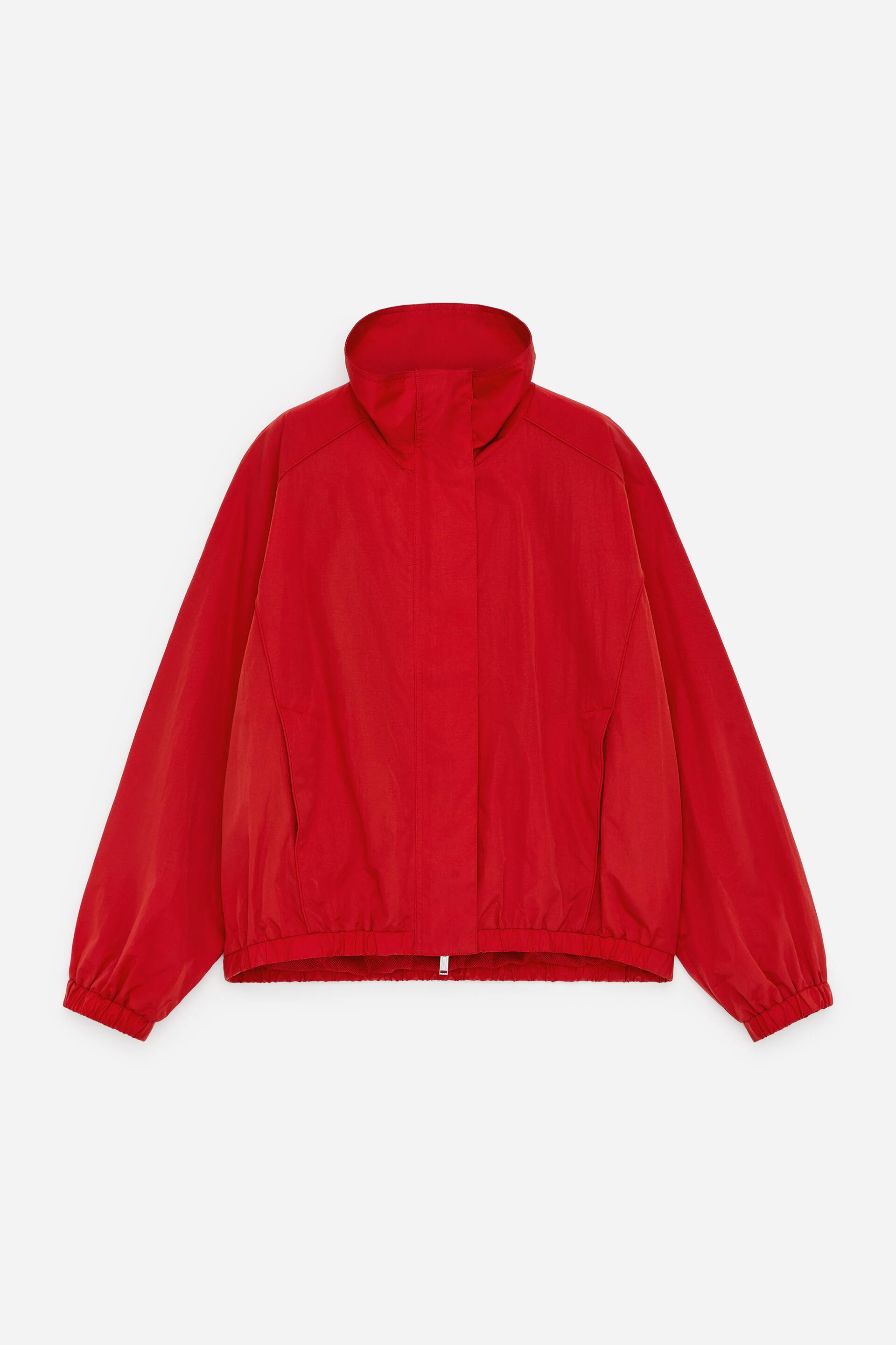 Agrandir l'image: Une veste rouge est présentée face avant, avec une forme carrée dotée de poignets et d'un ourlet élastiqués. Elle est conçue avec des manches raglan, un col cheminée, une patte de boutonnage à pression dissimulée sur une fermeture éclair frontale à double sens, et des poches latérales zippées.