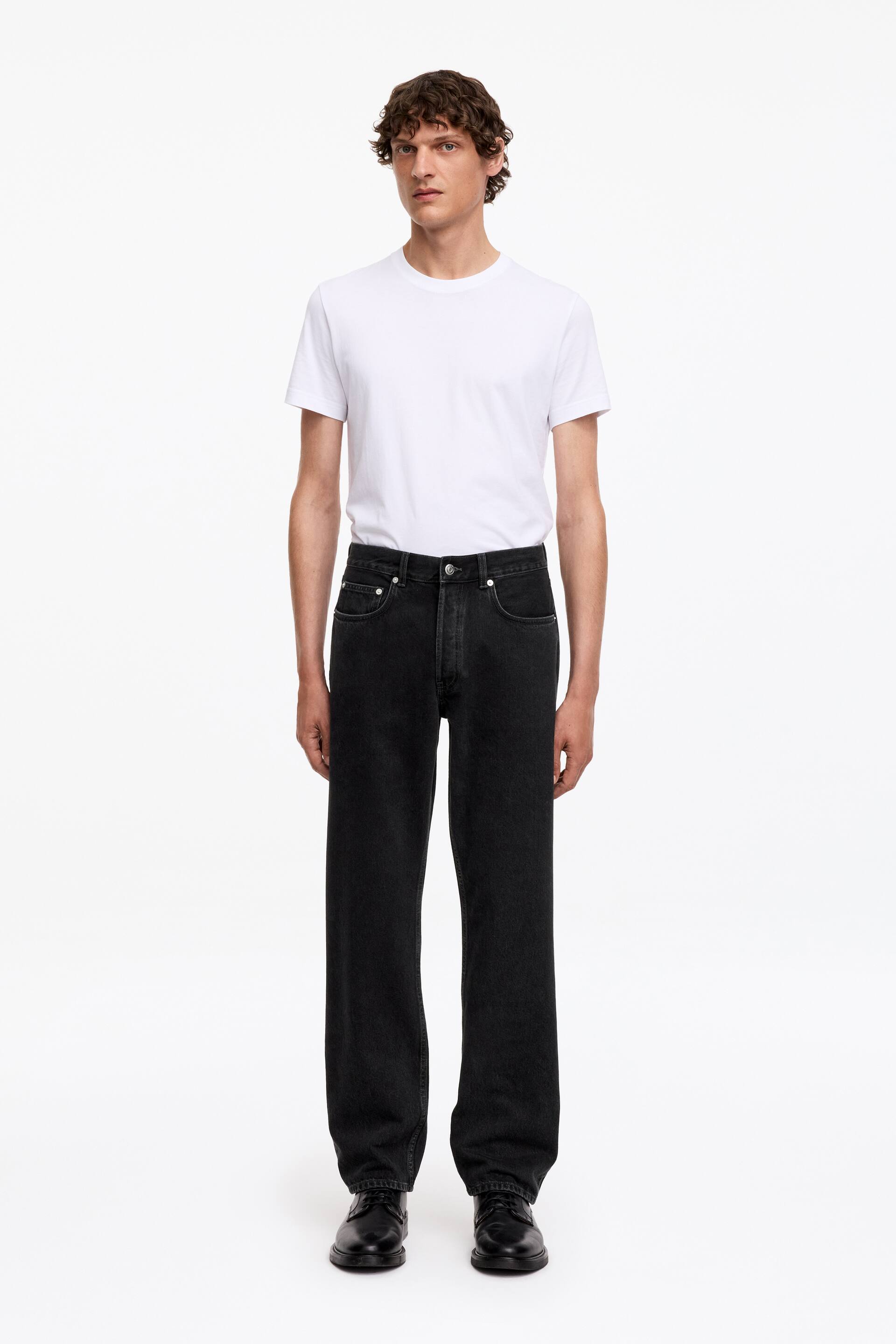 Agrandir l'image: Le mannequin porte un jean en denim noir OCEAN, présentant une coupe ample et droite avec des jambes de pleine longueur. Le jean affiche une taille mi-haute et une braguette à boutons, et est assorti d'un t-shirt blanc.