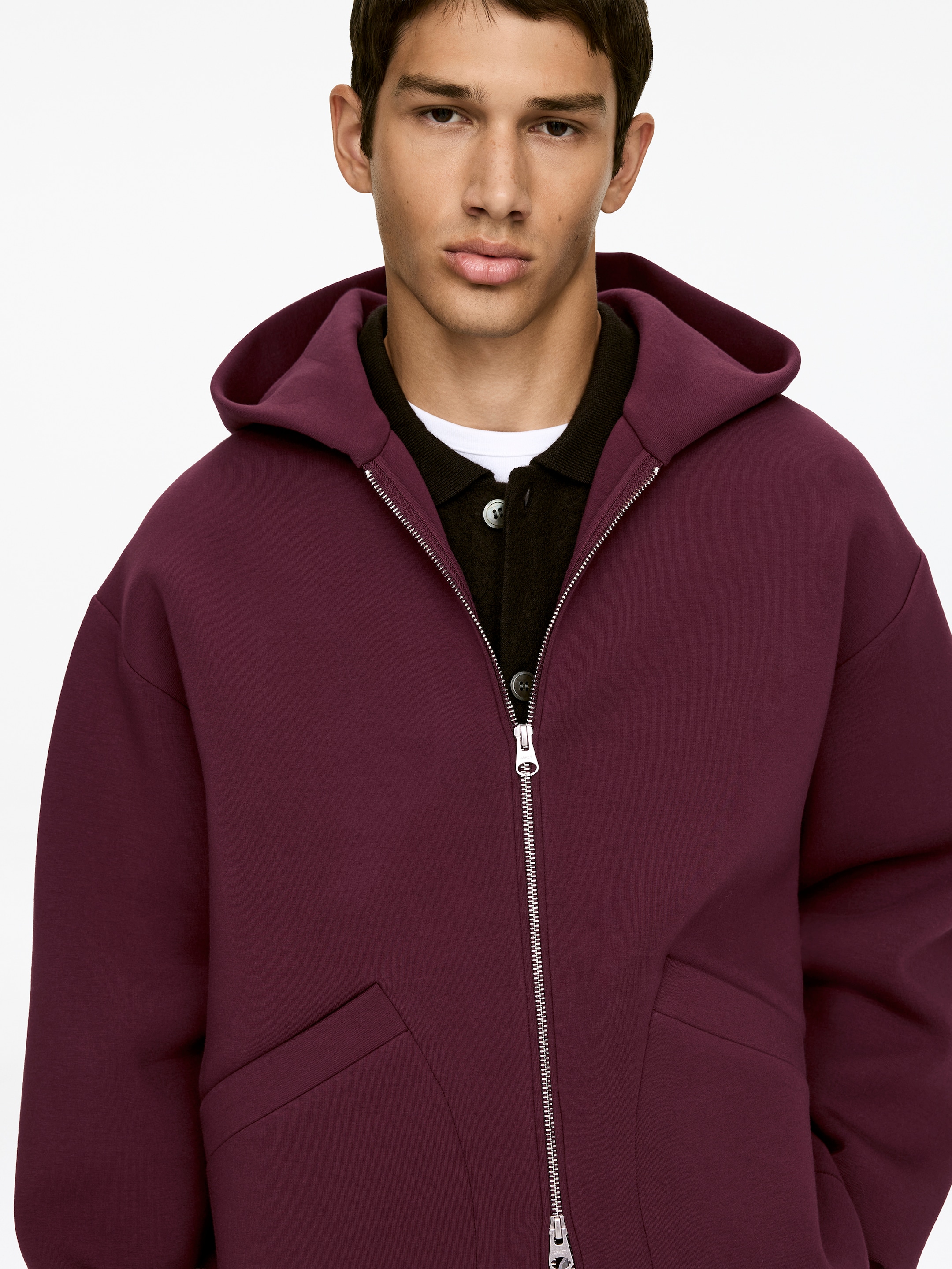 Ver imagen más grande: Una chaqueta con capucha color granate se presenta desde el frente, con una cremallera plateada de longitud completa y dos bolsillos welt en ángulo en la parte delantera. Está siendo usada sobre una camisa polo oscura y una camiseta interior blanca.