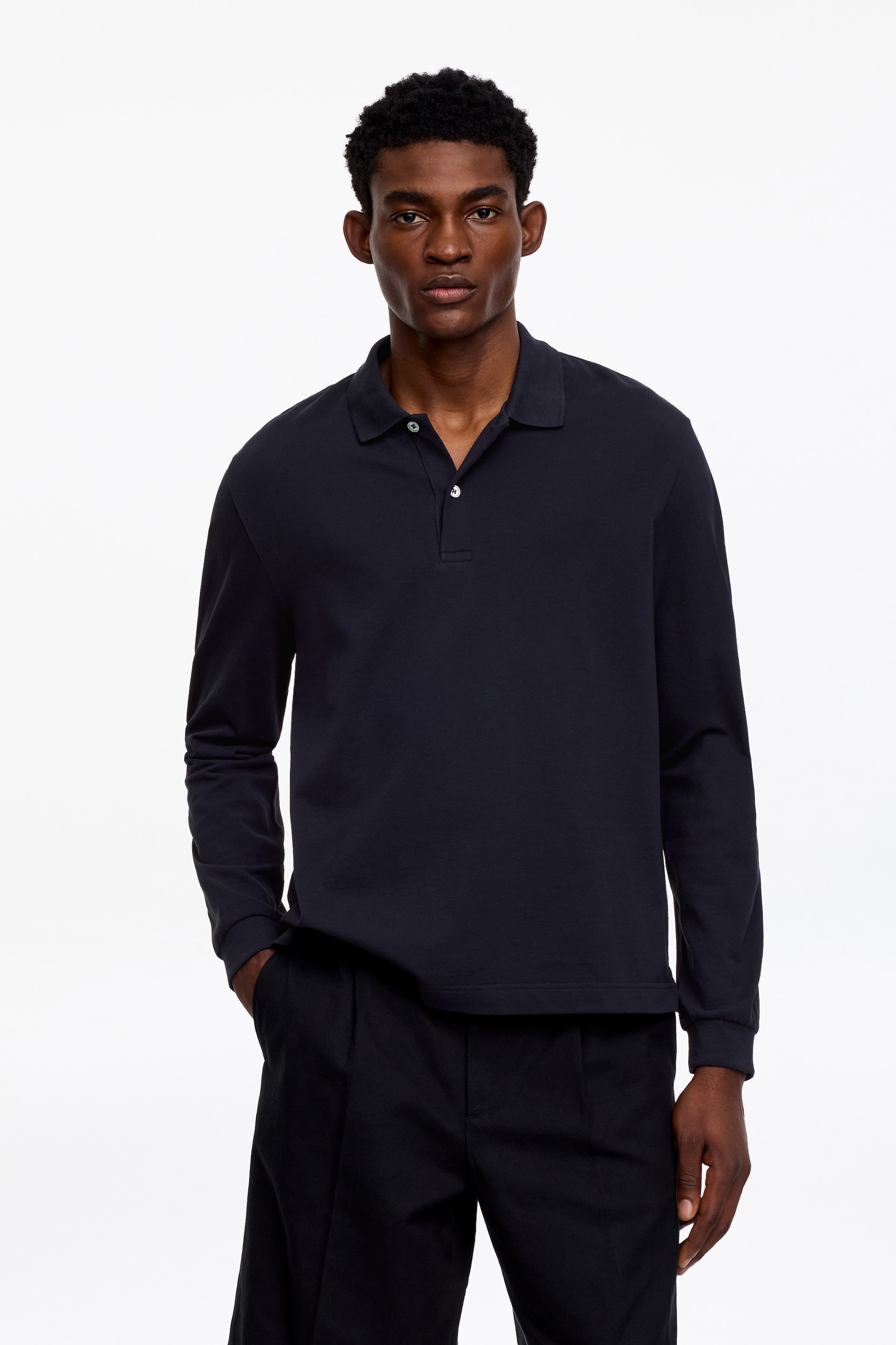 Ver imagen más grande: Una camisa polo de manga larga en azul oscuro presenta un clásico cuello polo y una tapeta de dos botones con botones claros. Muestra un ajuste relajado con puños lisos y un dobladillo recto.
