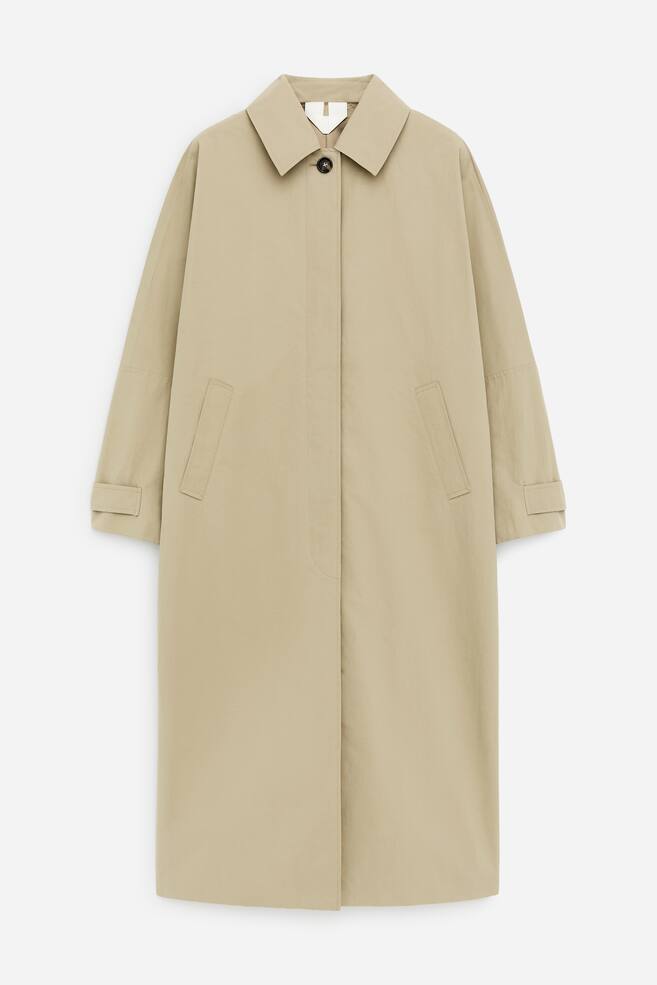 Ein beiger Trenchcoat wird VORNE präsentiert und verfügt über einen klassischen Umlegekragen, eine verdeckte Knopfleiste mit einem sichtbaren oberen Knopf, zwei schräge Leistentaschen, lange Ärmel mit umgeschlagenen Manschetten und eine lang geschnittene Silhouette. - 1