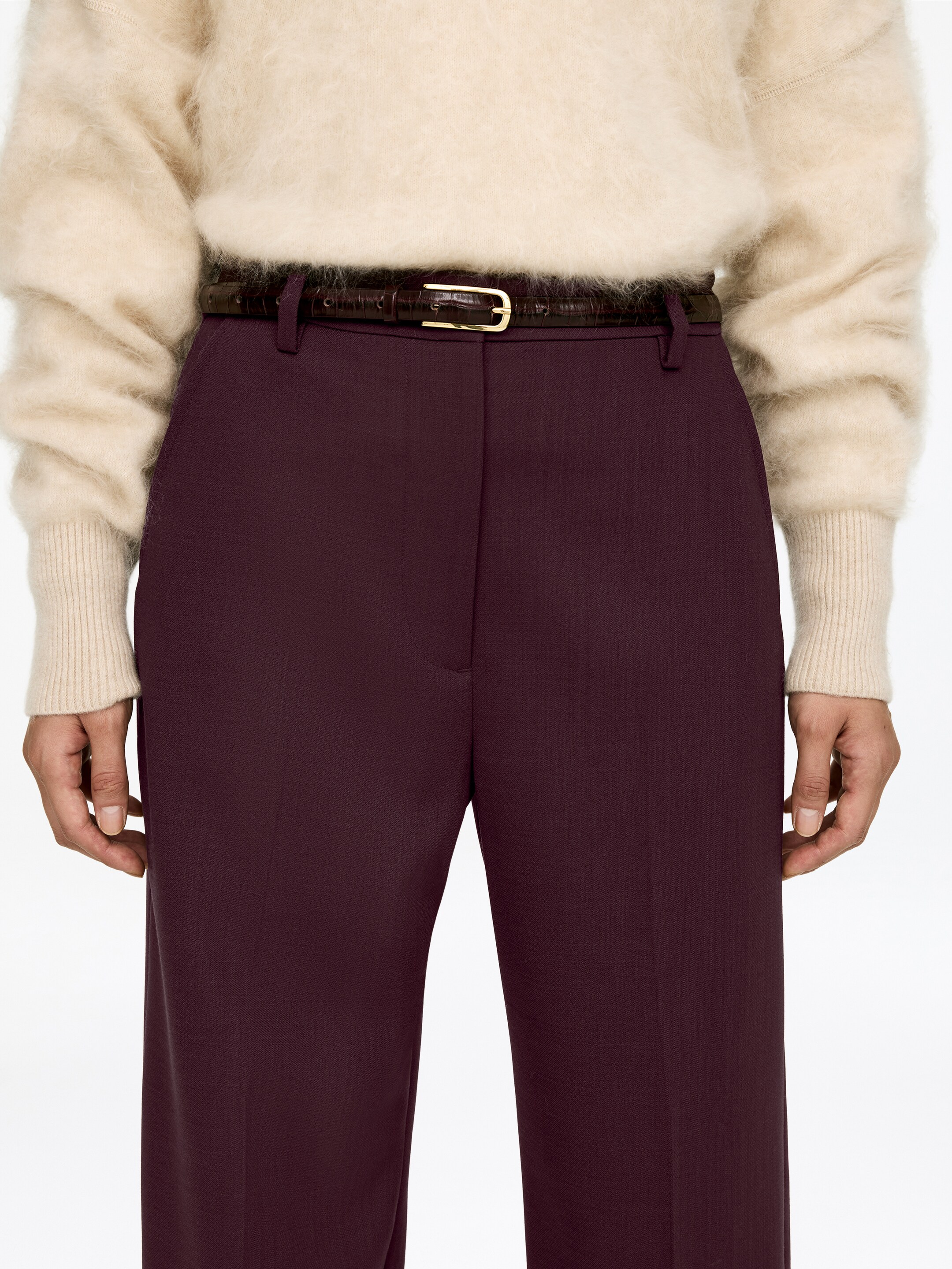 Visualizza immagine più grande: I pantaloni color marrone sono presentati frontalmente, caratterizzati da una trama intrecciata sottile, un design frontale piatto con passanti per cintura visibili e una piega verticale centrale lungo ciascuna gamba. Una cintura marrone scuro, con texture, con una fibbia rettangolare color oro è infilata attraverso la vita.