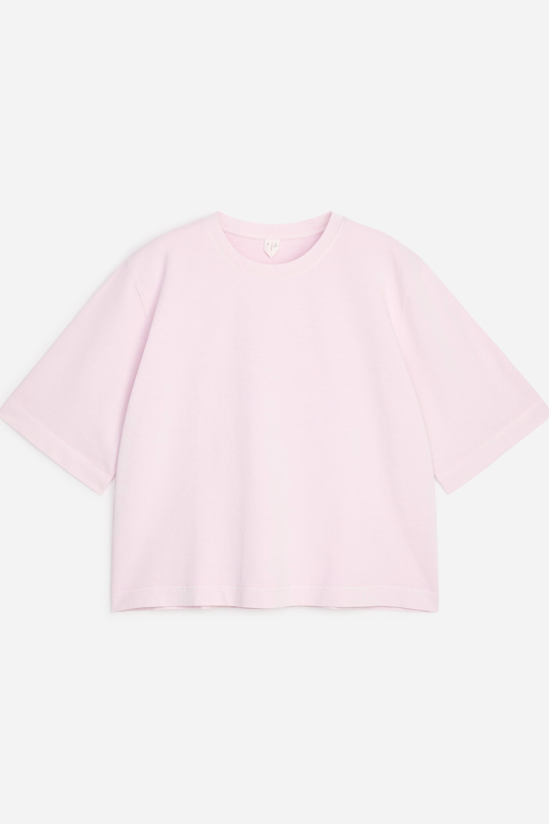 Ver imagen más grande: Una camiseta rosa claro está de frente, con cuello redondo, hombros caídos y mangas cortas extendidas. Presenta un dobladillo ligeramente recortado y un ajuste relajado y cuadrado.