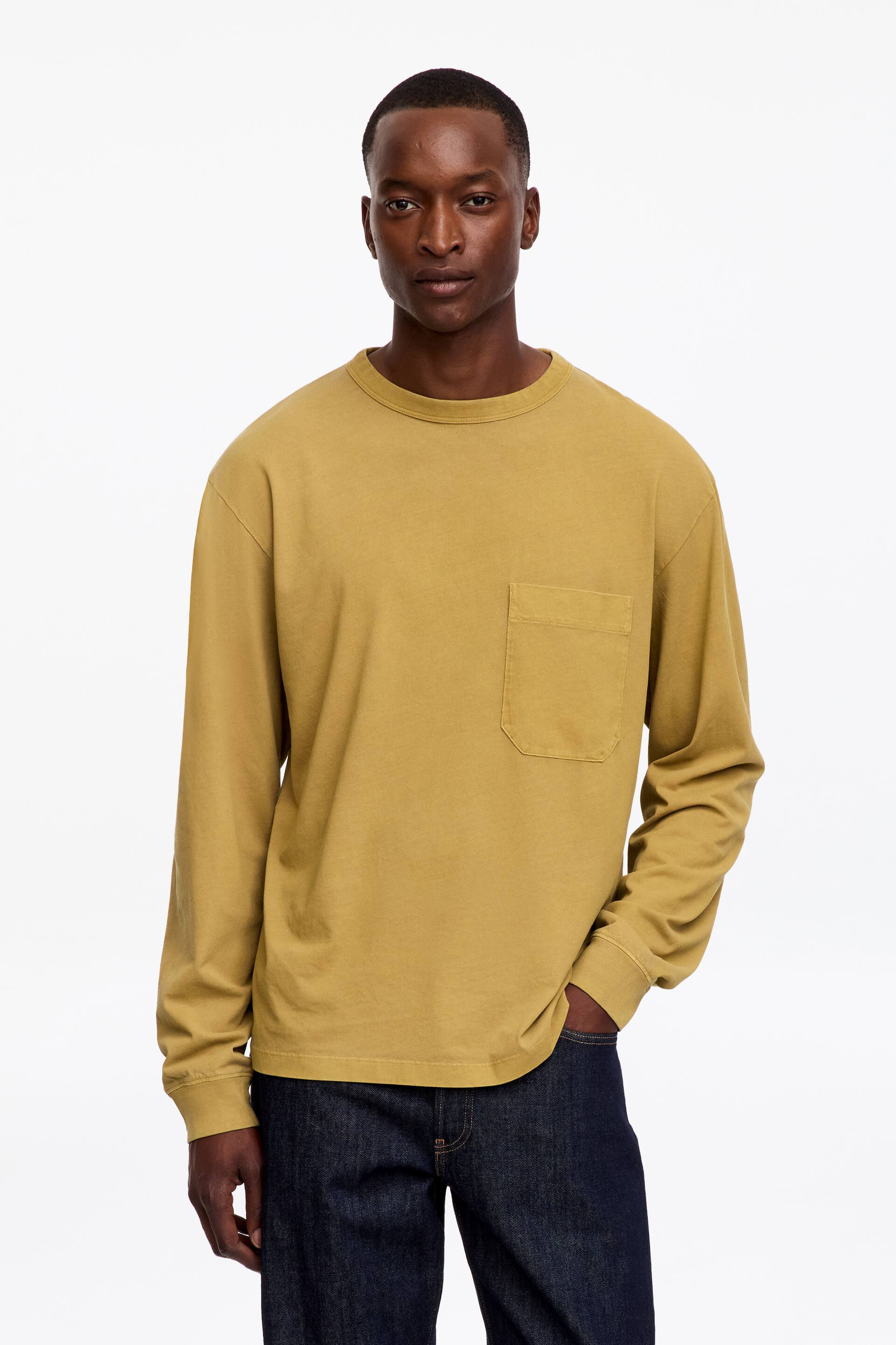 View larger image: A long-sleeved T-shirt featuring a washed vintage look, relaxed fit, crew neck, single chest pocket and ribbed cuffs is worn by the model. The model is standing with one hand resting in the pocket of dark wash jeans.