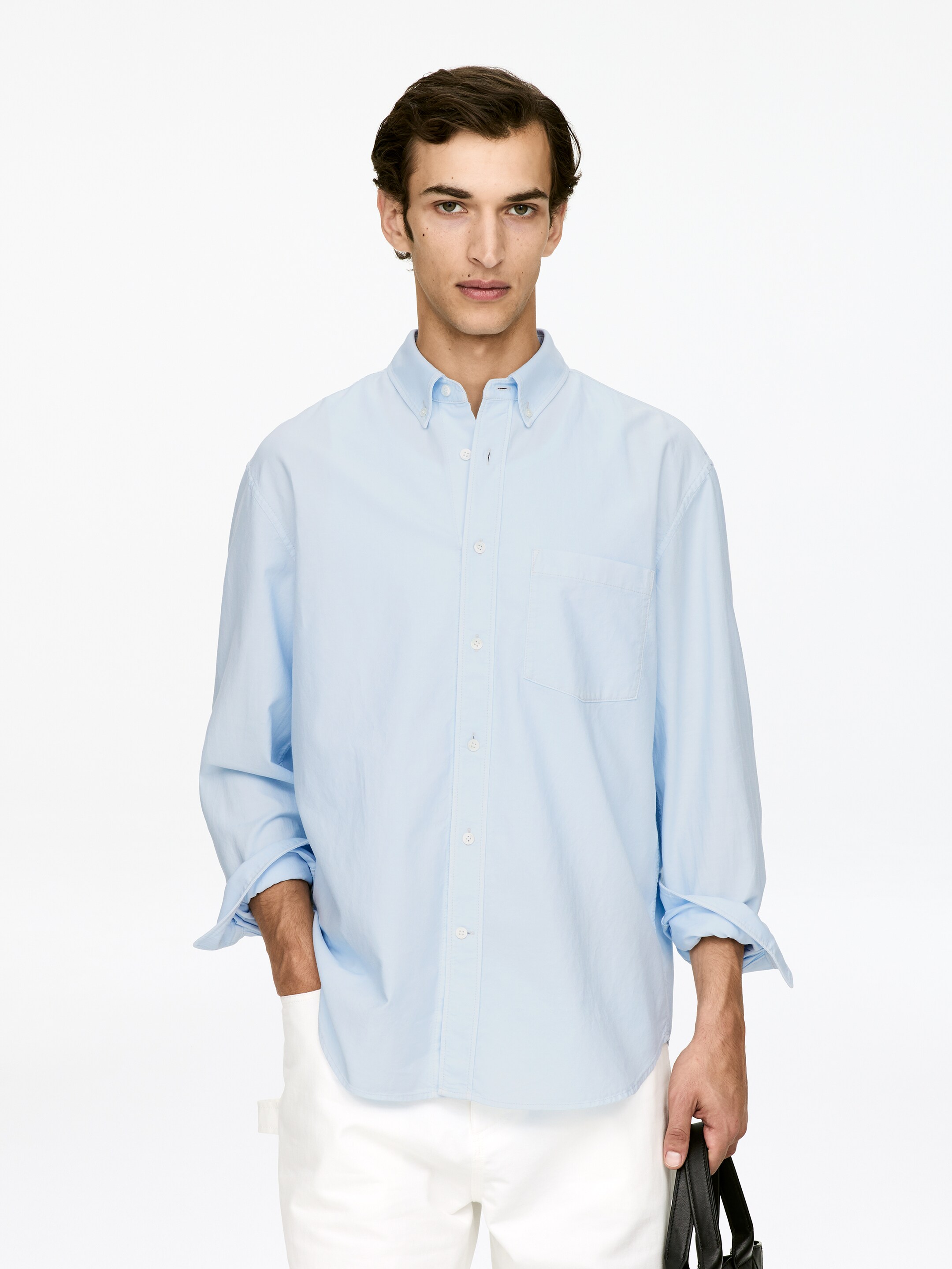 Agrandir l'image: Une chemise pour homme bleu clair est présentée de face. Elle est dotée d'un col boutonné, d'une patte de boutonnage complète avec des boutons blancs et d'une poche plaquée unique sur la poitrine gauche ; ses manches longues présentent un style retroussé, atteignant les avant-bras.