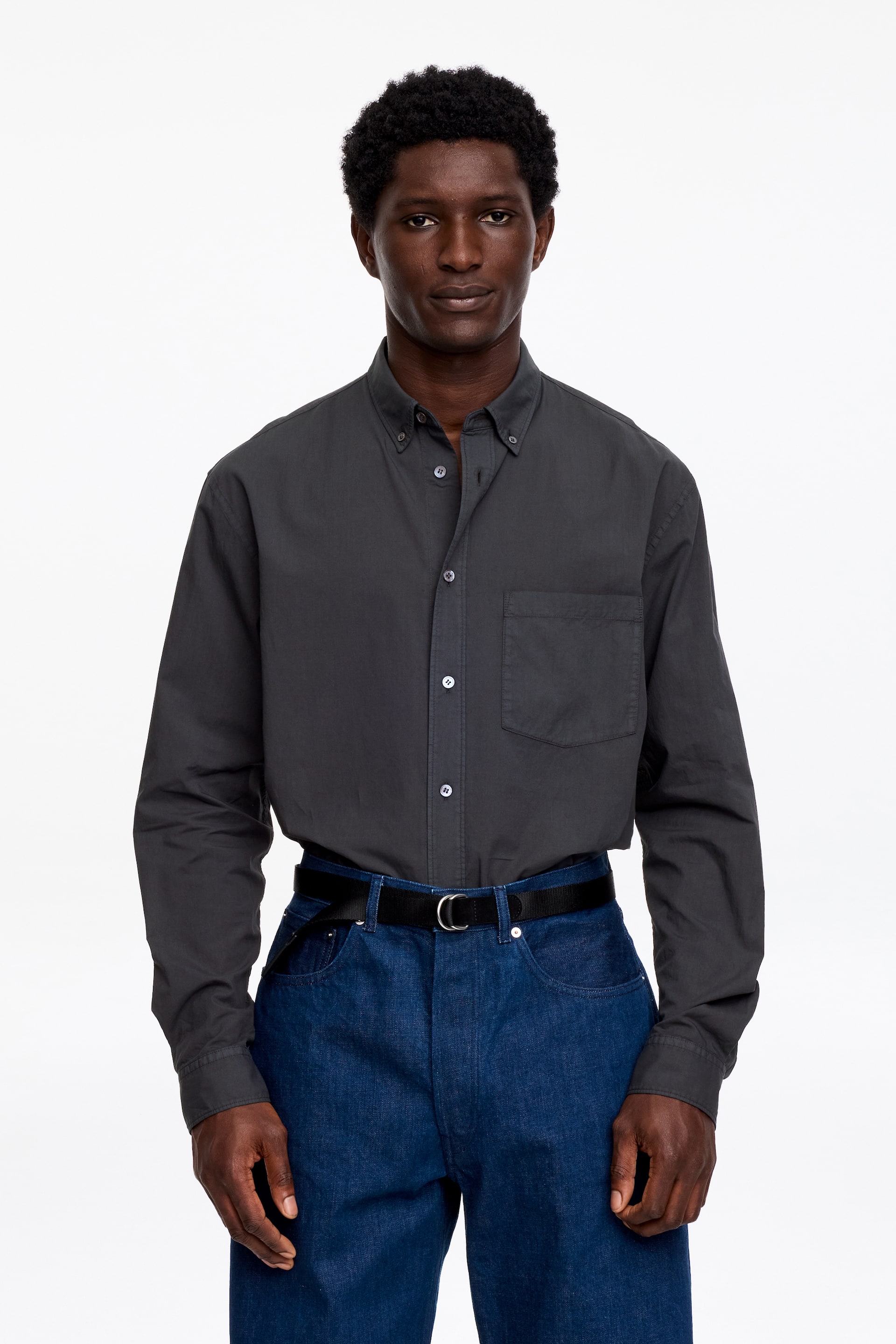 Zobrazit větší obrázek: Tmavě šedá košile s knoflíky má límec na knoflíky, plnou knoflíkovou légu se světlými knoflíky a náprsní kapsu na levé straně hrudi. Košile má také dlouhé rukávy s manžetami na knoflíky a je nošena zastrčená, pohled zepředu.