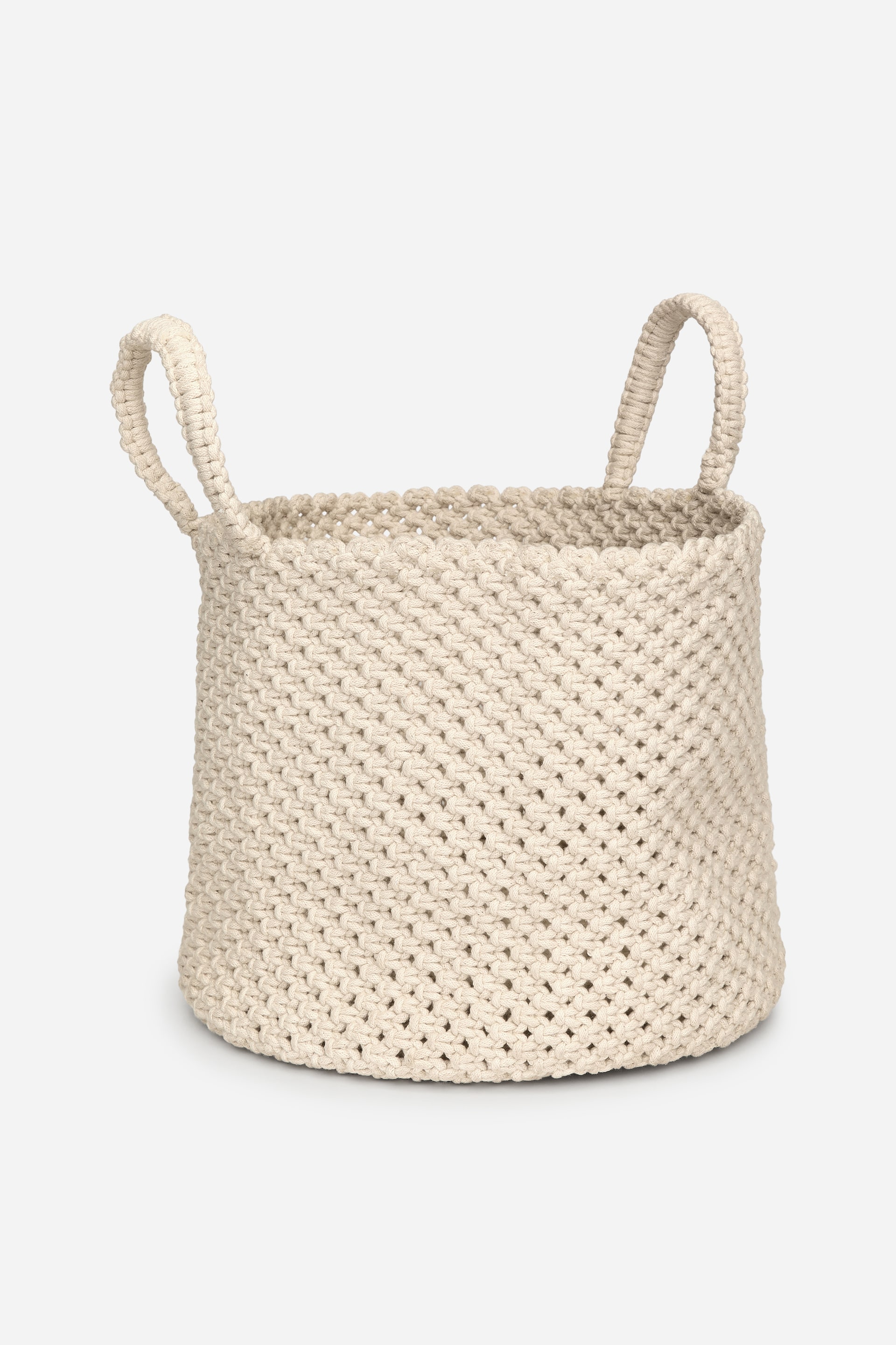 Größeres Bild anzeigen: Ein cremefarbener, zylindrischer Korb präsentiert ein grobes, im Makramee-Stil geknüpftes Design mit kleinen, offenen Lücken. Zwei robuste, geschlungene Griffe ragen vom Rand nach oben und sind aus demselben geknüpften Material gefertigt.