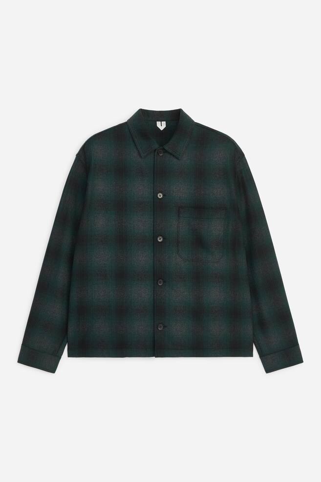 Ein langÃ¤rmliges Overshirt in dunkelgrÃ¼nem und schwarzem Karomuster ist von vorn zu sehen und zeigt einen Button-down-Verschluss, einen spitzen Kragen sowie eine einzelne aufgesetzte Brusttasche auf der linken Brust. Das KleidungsstÃ¼ck prÃ¤sentiert sich in einer lockeren Passform mit geradem Saum und schlichten Manschetten. - 1
