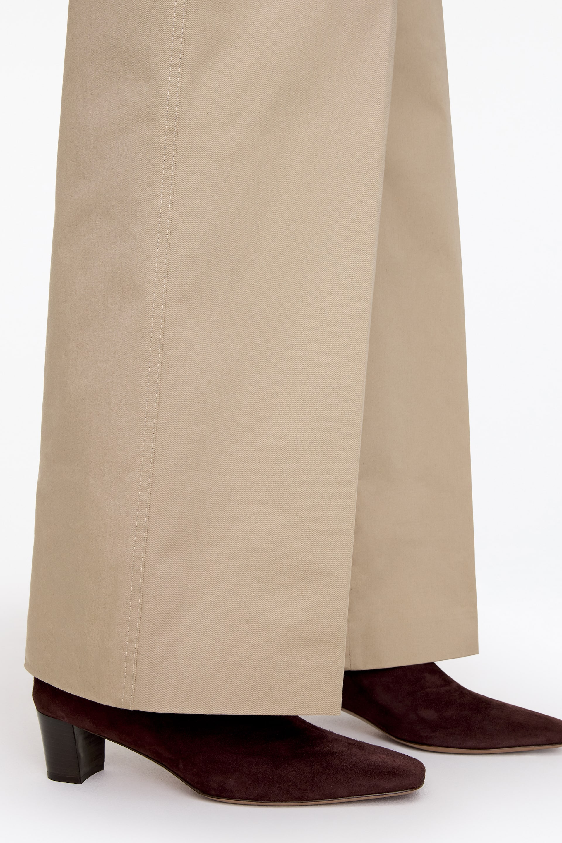 Grotere afbeelding bekijken: Donkerbruine suède enkellaarsjes met een zacht vierkante neus en lage blokhak worden gedragen door het model. De laarsjes worden gestyled onder een beige broek met wijde pijpen.