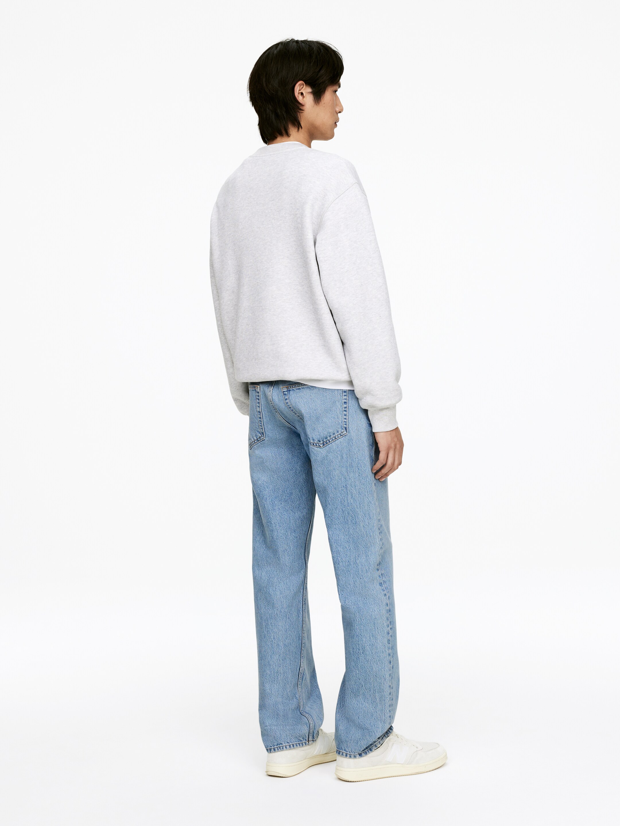Größeres Bild anzeigen: Ein hellgraues Sweatshirt mit Rundhalsausschnitt wird getragen, sein lockerer Schnitt und die gerippten Bündchen sind von hinten und von der rechten Seite sichtbar. Es wird mit hellblauen Jeans mit geradem Bein und cremeweißen Low-Top-Sneakern kombiniert.