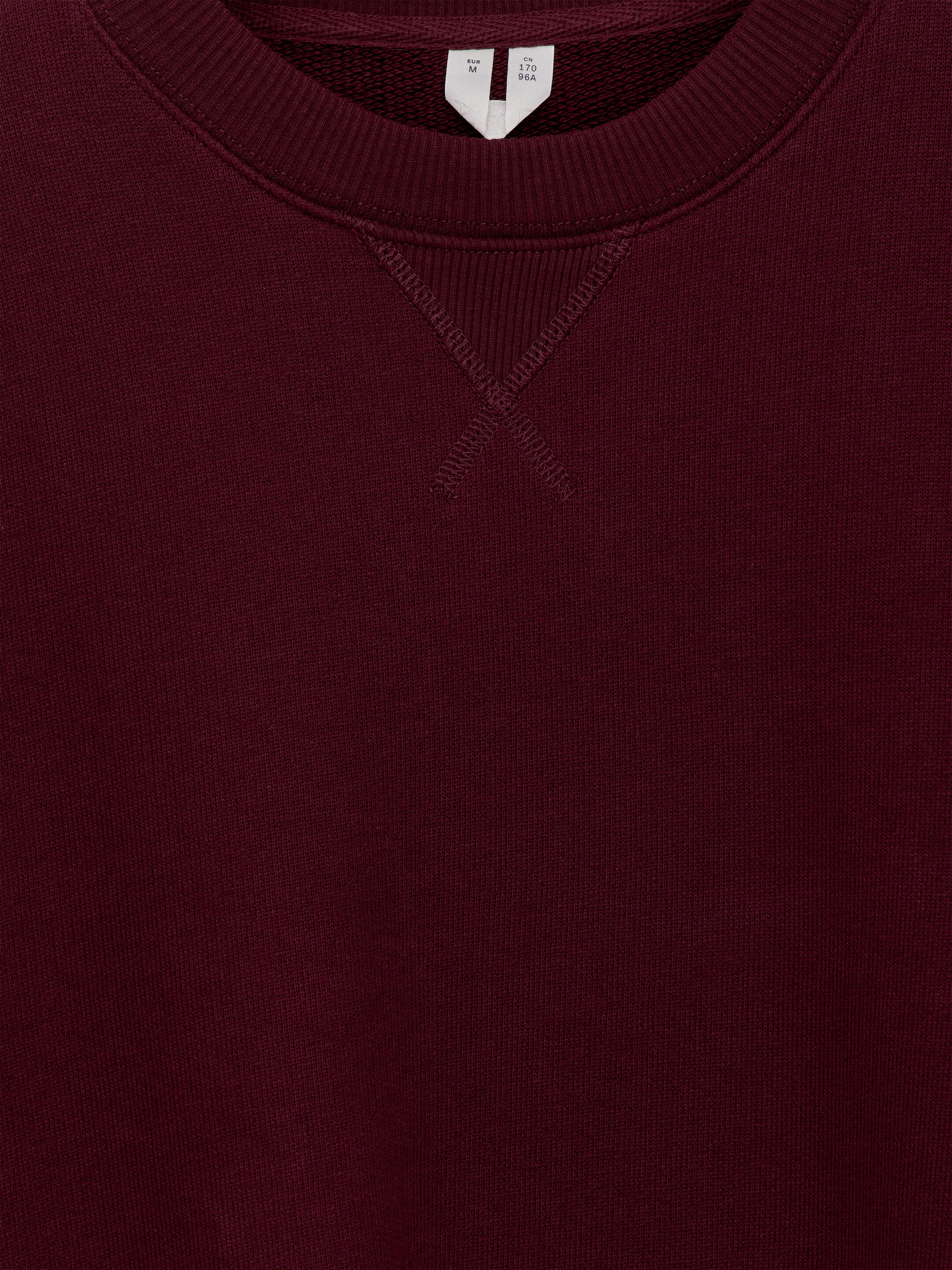 Größeres Bild anzeigen: Ein bordeauxrotes Sweatshirt verfügt über einen gerippten Rundhalsausschnitt mit einem sichtbaren V-Stich-Detail am vorderen Halsausschnitt.
