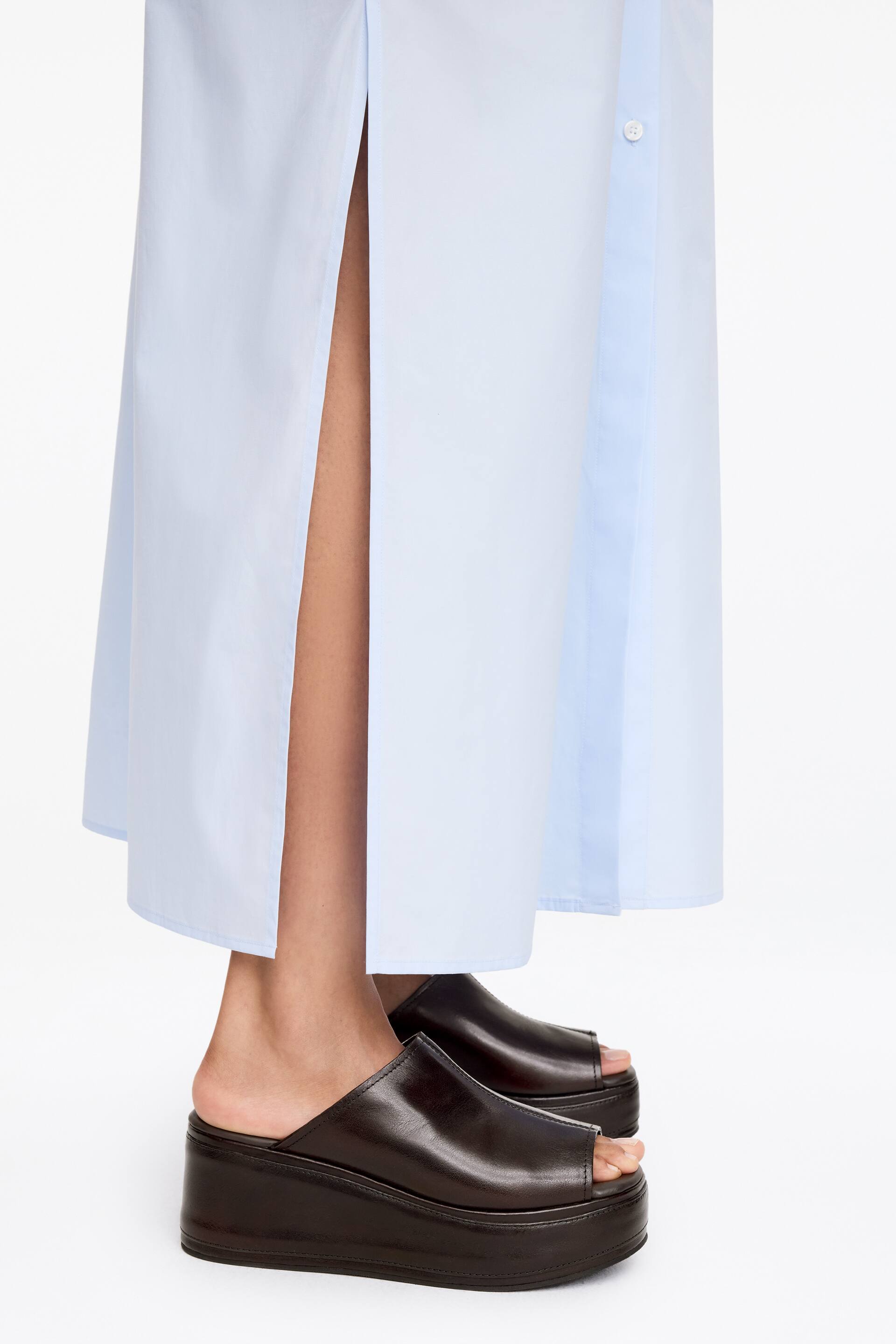 Näytä suurempi kuva: Tummanruskeat flatform-sandaalit, joissa on peep-toe ja suoraleikkauksinen päällinen pyöristetyllä kärjellä, ovat mallin jalassa. Nämä sandaalit on yhdistetty vaaleansiniseen mekkoon, jossa on sivuhalkio.