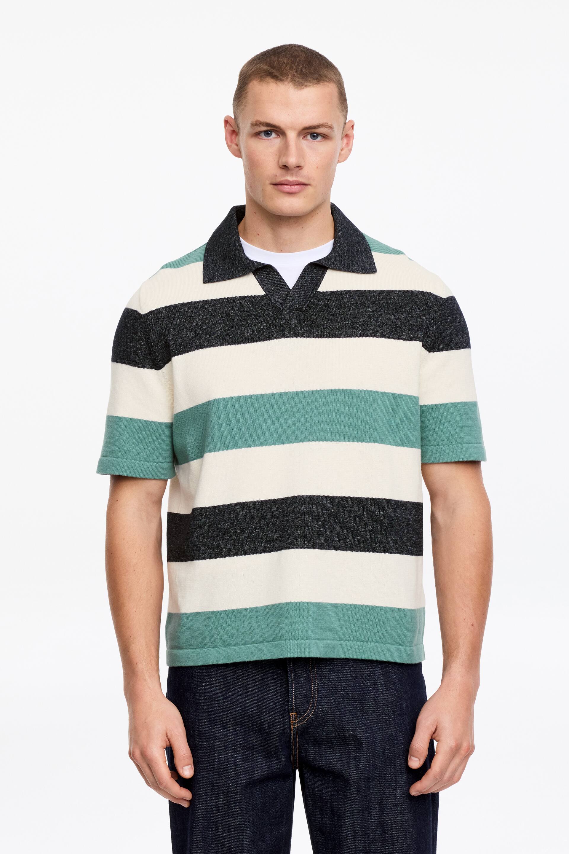 Größeres Bild ansehen: Ein gestreiftes Polohemd mit kurzen Ärmeln und horizontalen Streifen in Schwarz, Off-White und Teal. Es ist mit einem dunklen, gespreizten Kragen und einem V-Ausschnitt gestaltet, wobei ein weißes Rundhals-T-Shirt darunter sichtbar ist.