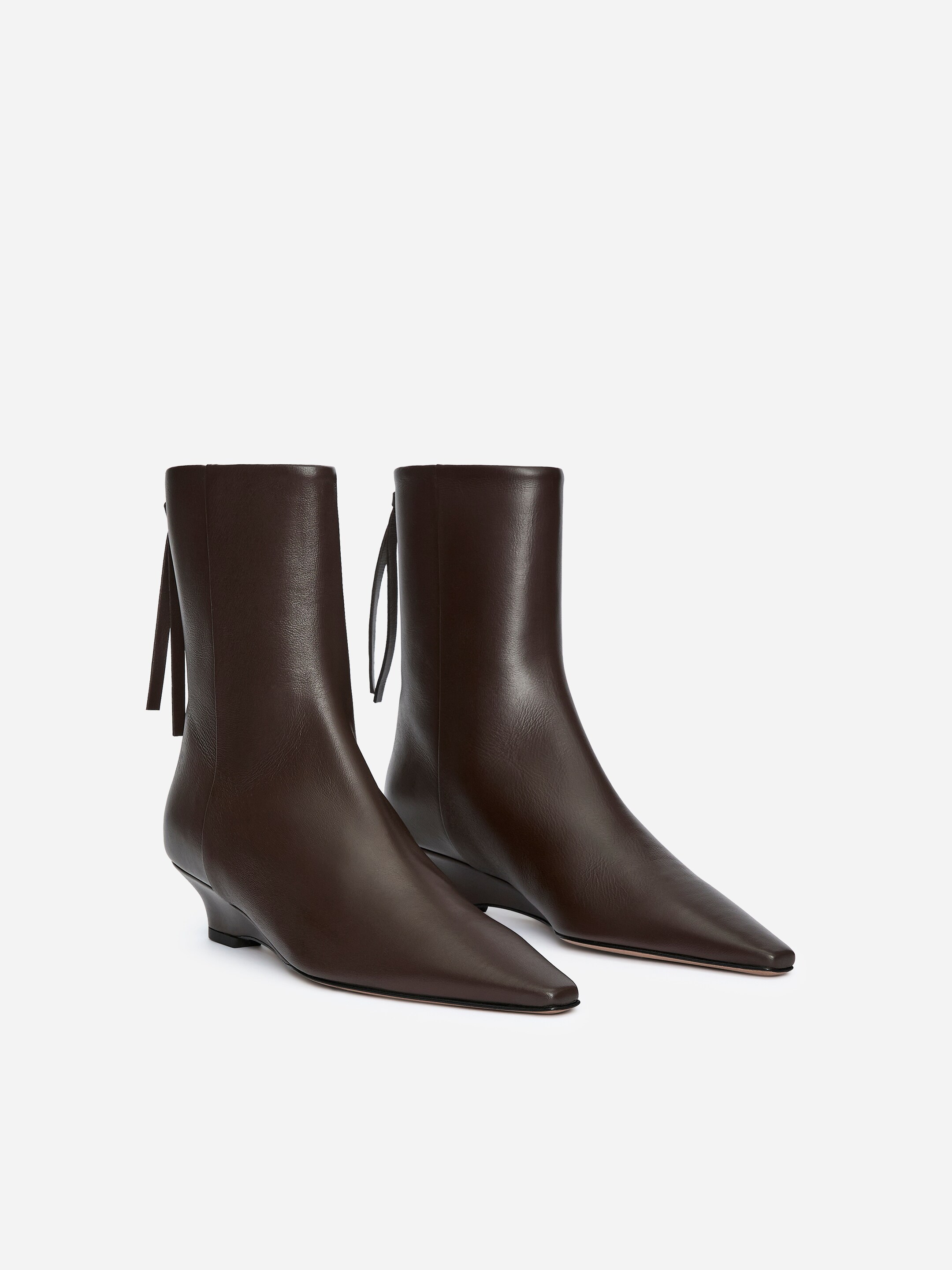 Se større billede: To mørkebrune læder ankelstøvler præsenteres, med slanke spidse tæer og lave, udvidede hæle. Tynde dekorative snørebånd er synlige på bagsiden af hver støvles skaft, med den venstre støvle vinklet for at fremvise sin sideprofil.