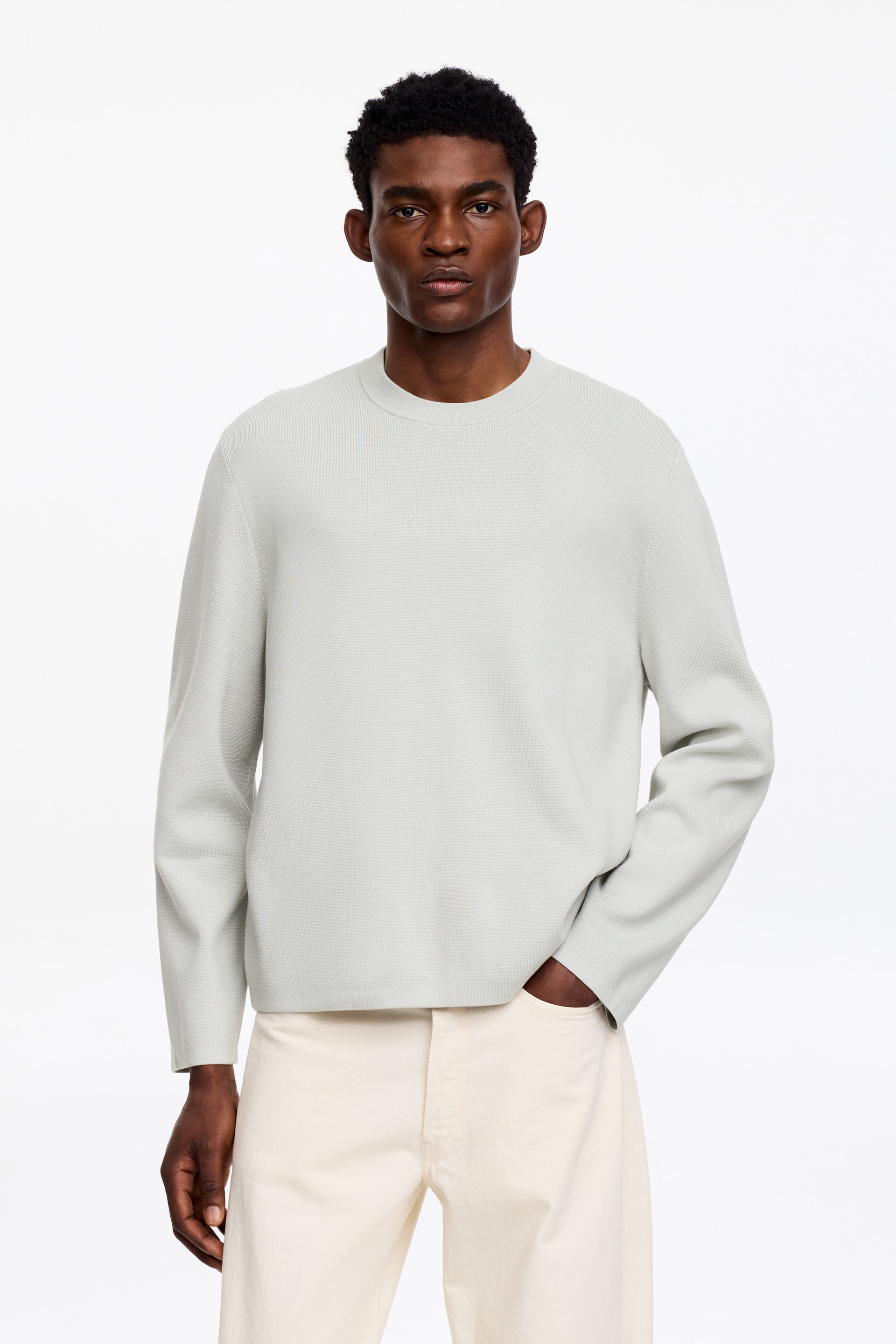 Grösseres Bild ansehen: Ein hellgrau-grüner Pullover mit Rundhalsausschnitt wird nach vorne getragen. Er verfügt über lange Ärmel, eine glatte Textur und eine entspannte Passform, mit einem geraden Saum, der oberhalb der Taille sitzt.
