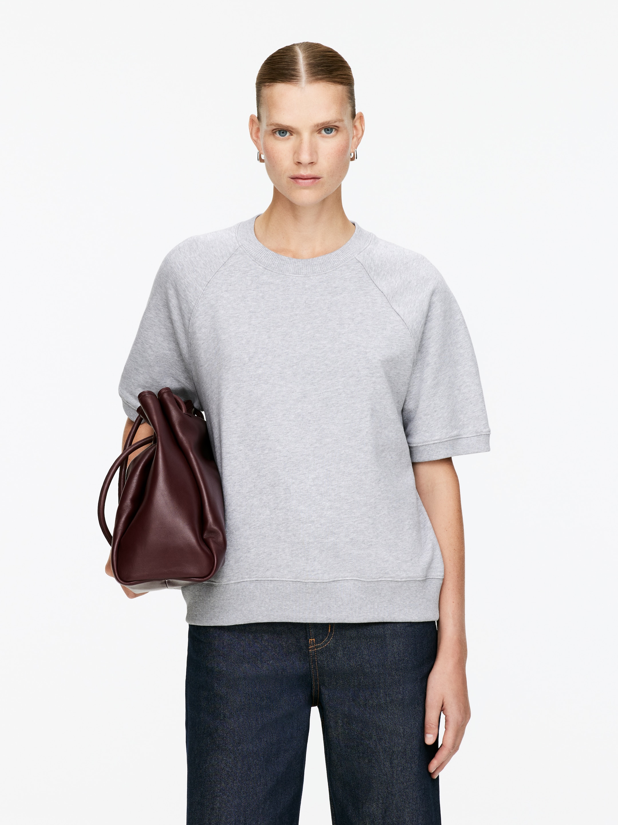 Agrandir l'image: Un sweat-shirt à manches courtes gris clair est porté, avec un col rond côtelé et des coutures raglan. Il est détaillé avec des poignets côtelés sur ses manches courtes et un ourlet côtelé, offrant une coupe décontractée.