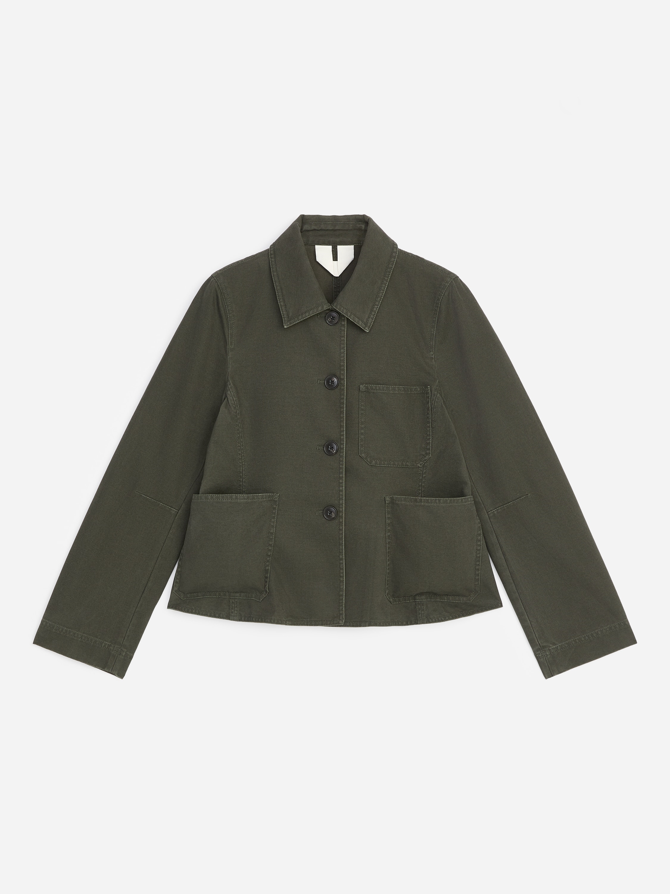 La modelo lleva una chaqueta de lona de algodÃ³n verde oscuro con cuello puntiagudo, cierre frontal de botones, bolsillos de parche y bajo evasÃ©. La chaqueta se combina con una camiseta blanca y pantalones negros de pernera ancha.