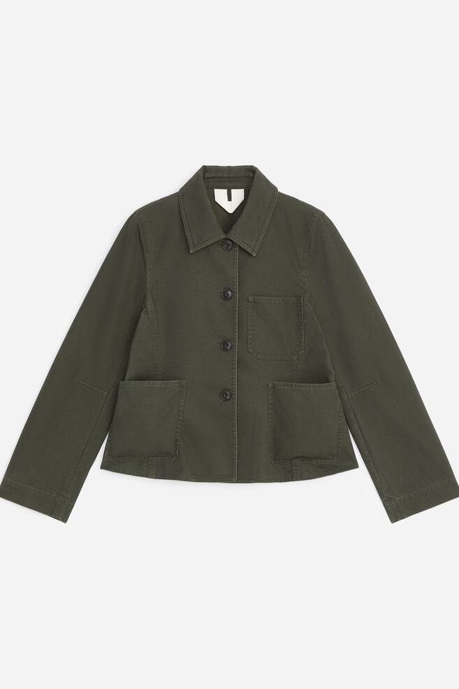 This dark green cotton canvas jacket is shown from the front, featuring a structured silhouette with a subtle peplum hem. It features a classic pointed collar, a four-button front fastening, one chest patch pocket, and two large lower patch pockets. - 1
