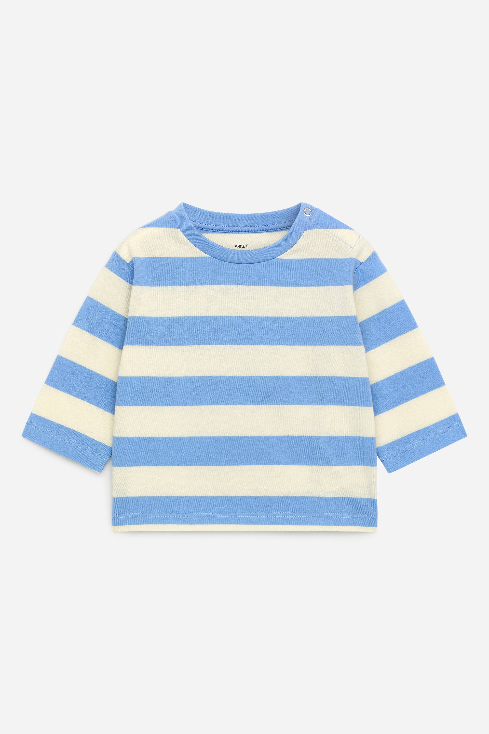 Ingrandisci l'immagine: Una maglia a maniche lunghe è mostrata nella sua vista FRONTALE, caratterizzata da strisce orizzontali blu e bianco sporco. È progettata con un collo rotondo, un unico bottone a pressione sulla spalla sinistra e piccoli spacchi sulle cuciture laterali.