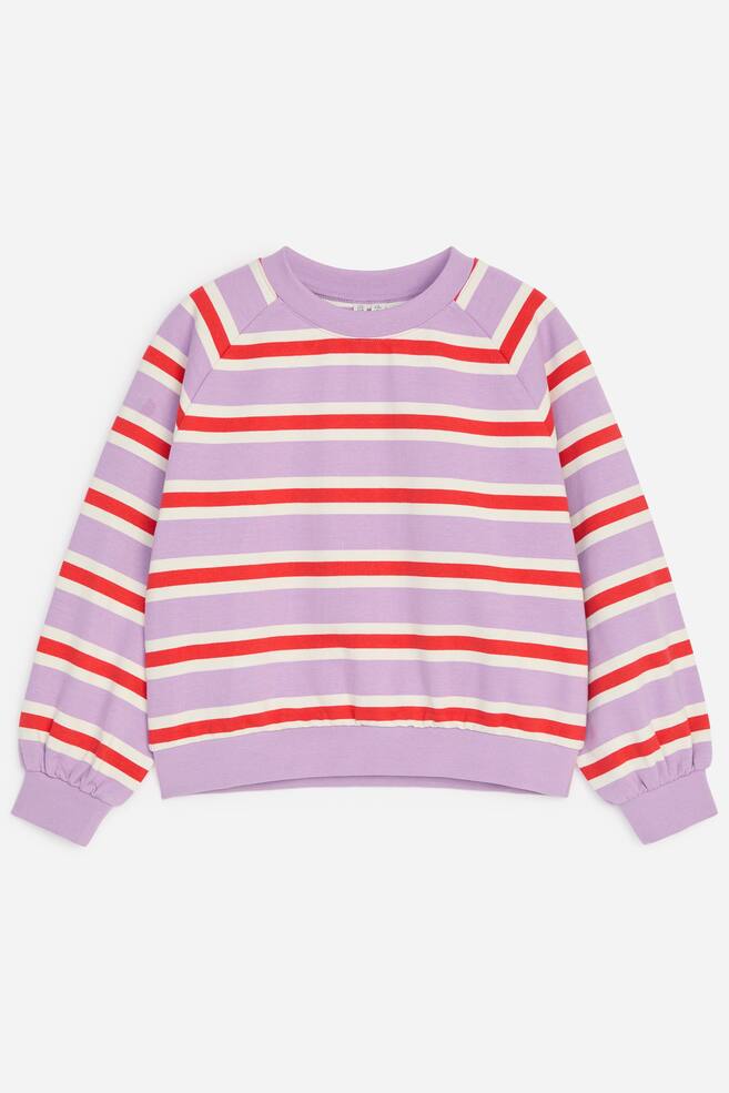 Uma sweatshirt de corte quadrado e ligeiramente oversized estÃ¡ disposta na horizontal, vista de frente, apresentando riscas horizontais em lavanda, vermelho e creme. O design destaca mangas raglan, gola redonda canelada e acabamentos canelados na bainha e nos punhos. - 1