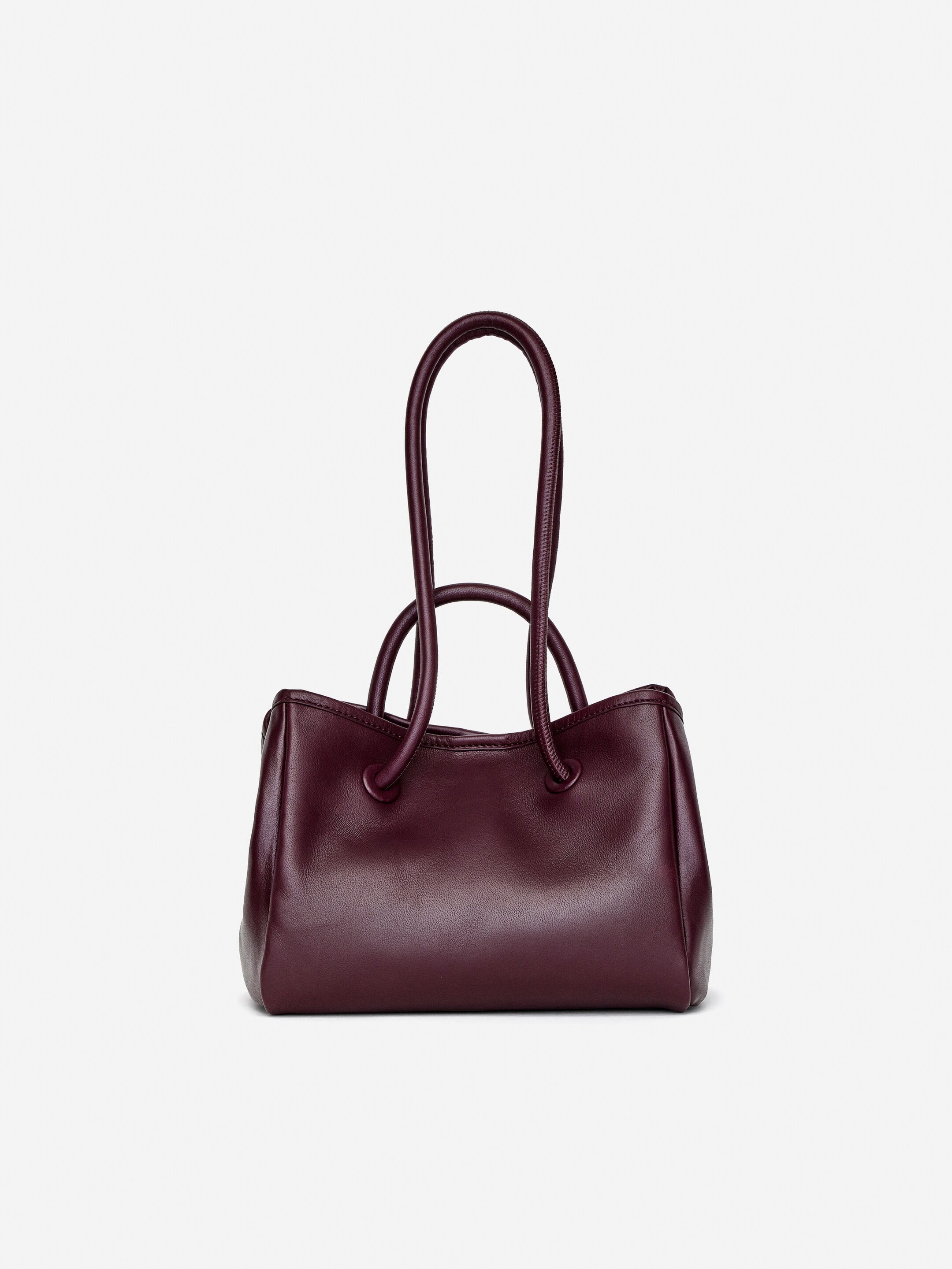 Visualizza immagine più grande: Una borsa a tracolla in pelle bordeaux scuro presenta la sua parte anteriore, caratterizzata da due manici corti e arrotondati e due lunghe tracolle tubolari. Le tracolle tubolari scorrono attraverso occhielli alla base dei manici superiori, con una tracolla che presenta una sottile texture a coste.