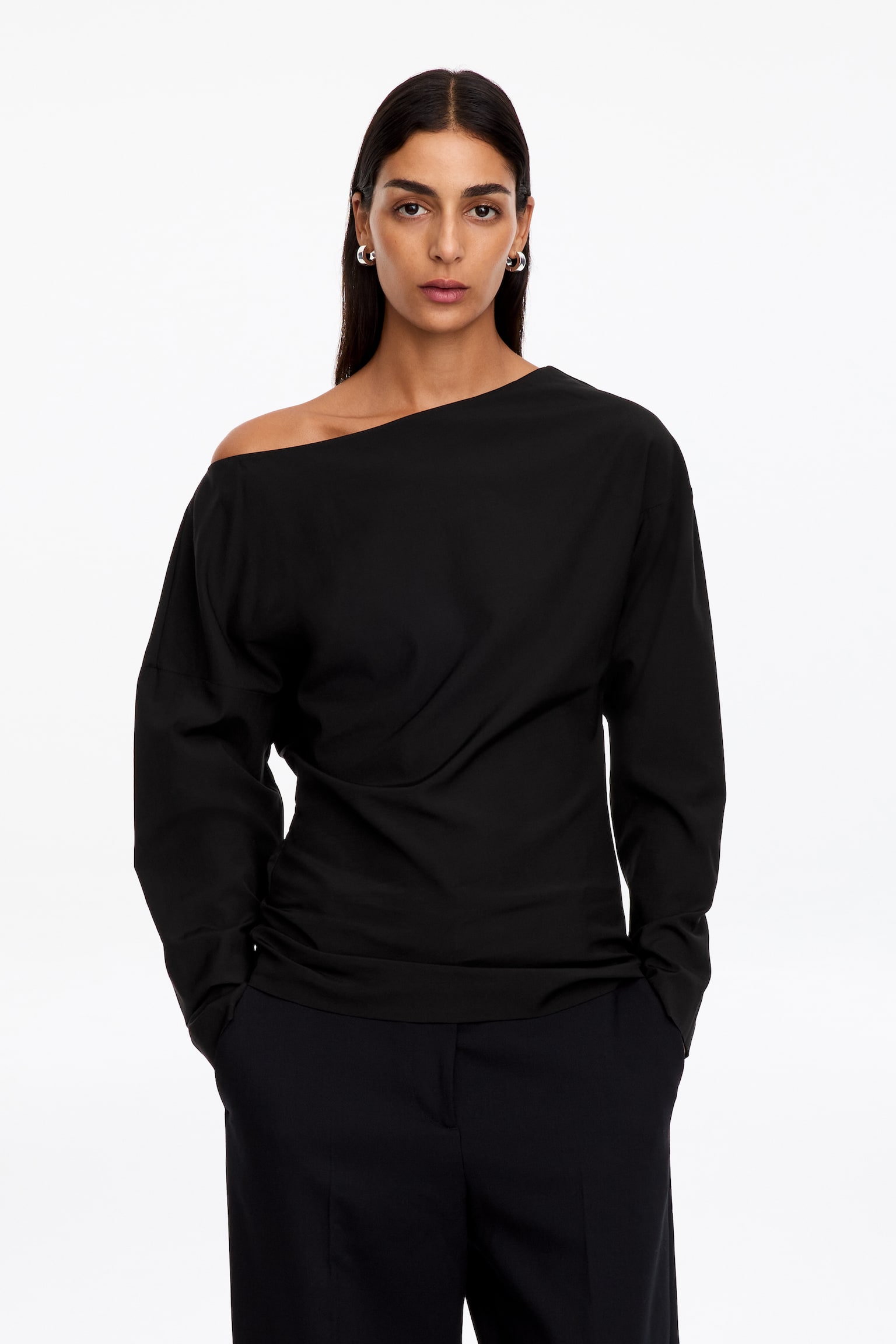 Una blusa negra de manga larga aparece de frente, mostrando un amplio escote barco y hombros caÃdos que dan paso a unas mangas largas y holgadas. La prenda presenta un bajo recto y una confección en tejido suave y ligero. - 1