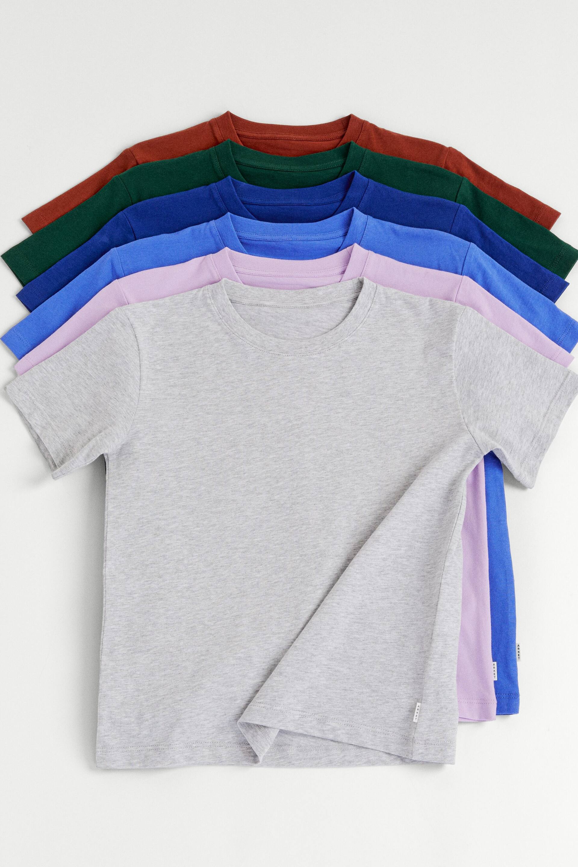 Agrandir l'image: Plusieurs t-shirts à col rond et à manches courtes sont disposés en éventail, avec un t-shirt gris clair au premier plan, de face, recouvrant partiellement des t-shirts lavande, bleus, vert foncé et rouille.