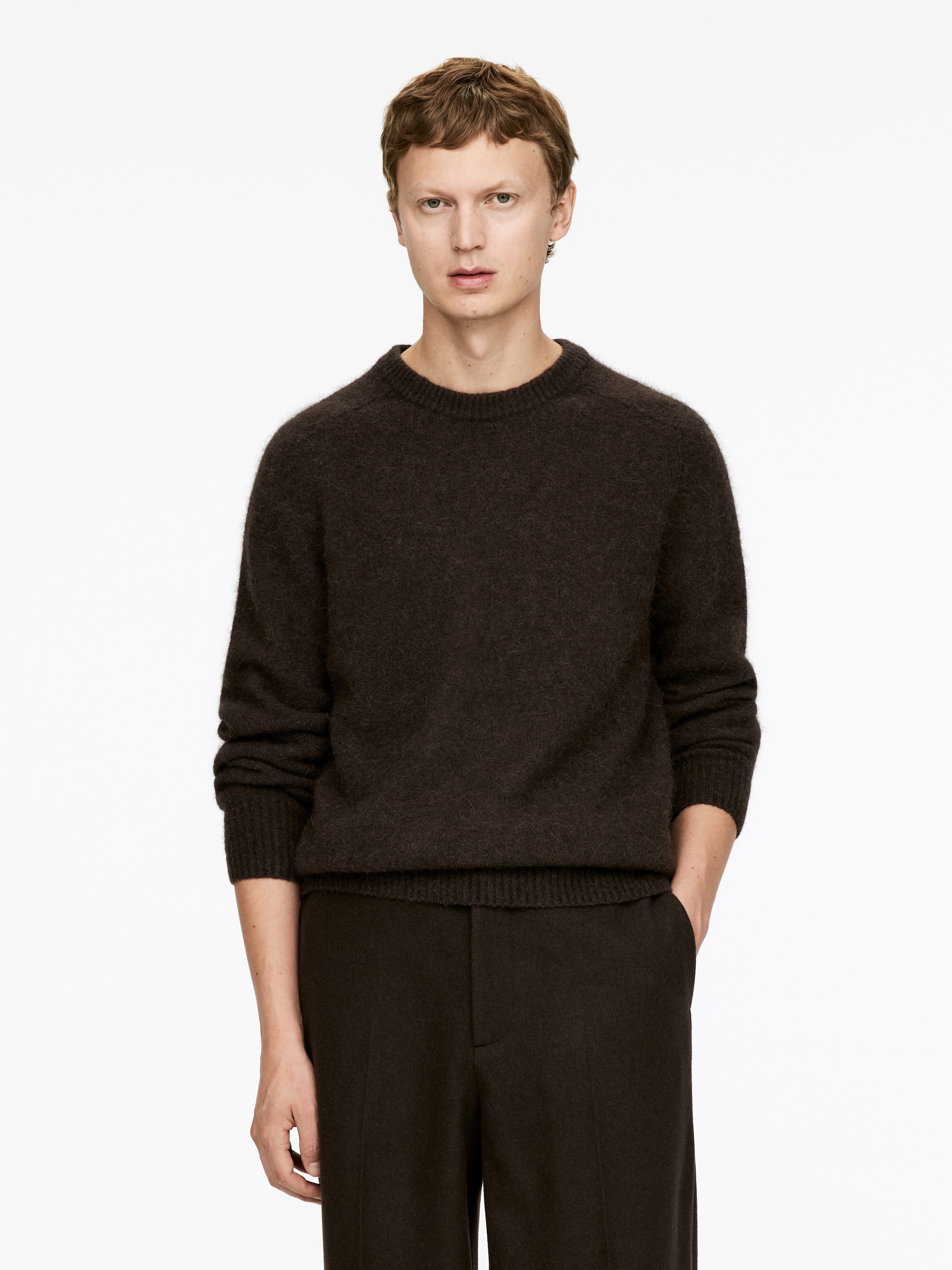 Größeres Bild anzeigen: Ein dunkelbrauner Pullover mit Rundhalsausschnitt wird von vorne präsentiert und zeigt eine sichtbar gebürstete Textur. Der Pullover weist gerippte Bündchen und einen gerippten Saum auf und wird über passenden dunkelbraunen Hosen getragen.