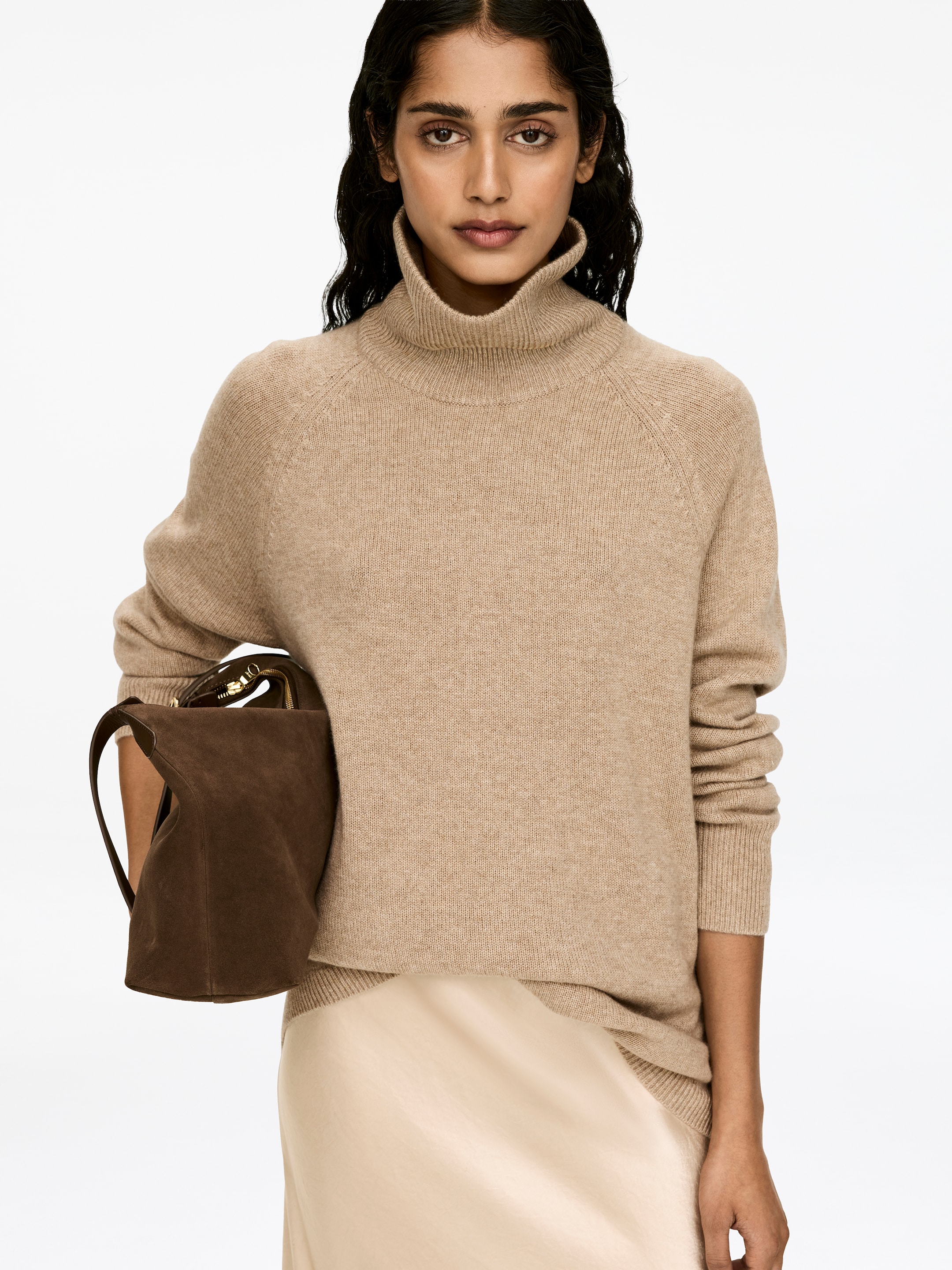 Visa större bild: En beige polotröja med raglanärmar och ribbade detaljer bärs av modellen. Modellen håller en brun väska och har en ljusfärgad kjol, som är synlig under tröjan.