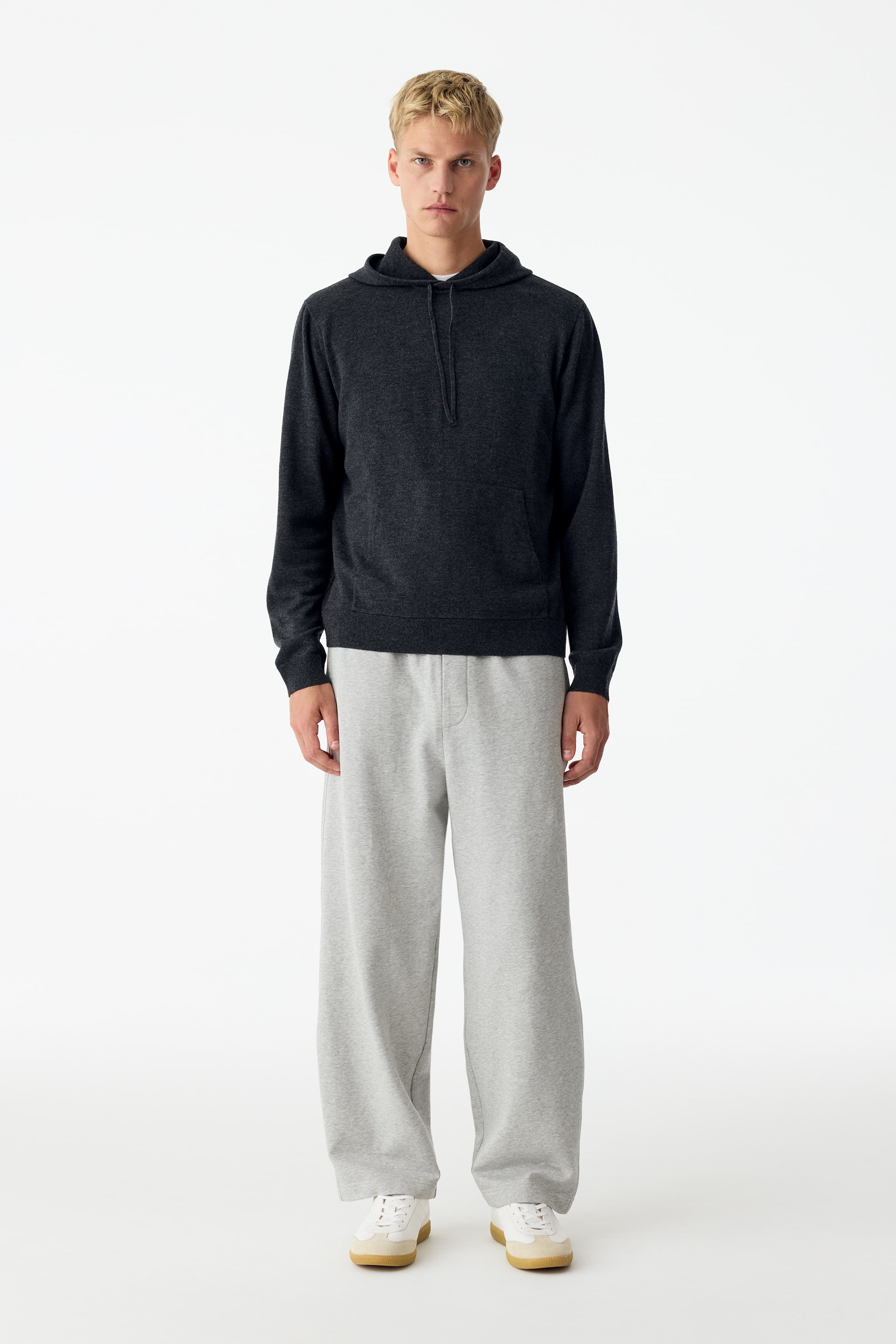 View larger image: Light grey relaxed-fit jersey trousers are being worn by the model, featuring a slightly tapered leg, an elasticated waistband, and a faux fly detail. The trousers are paired with a dark grey hooded sweatshirt and white trainers.