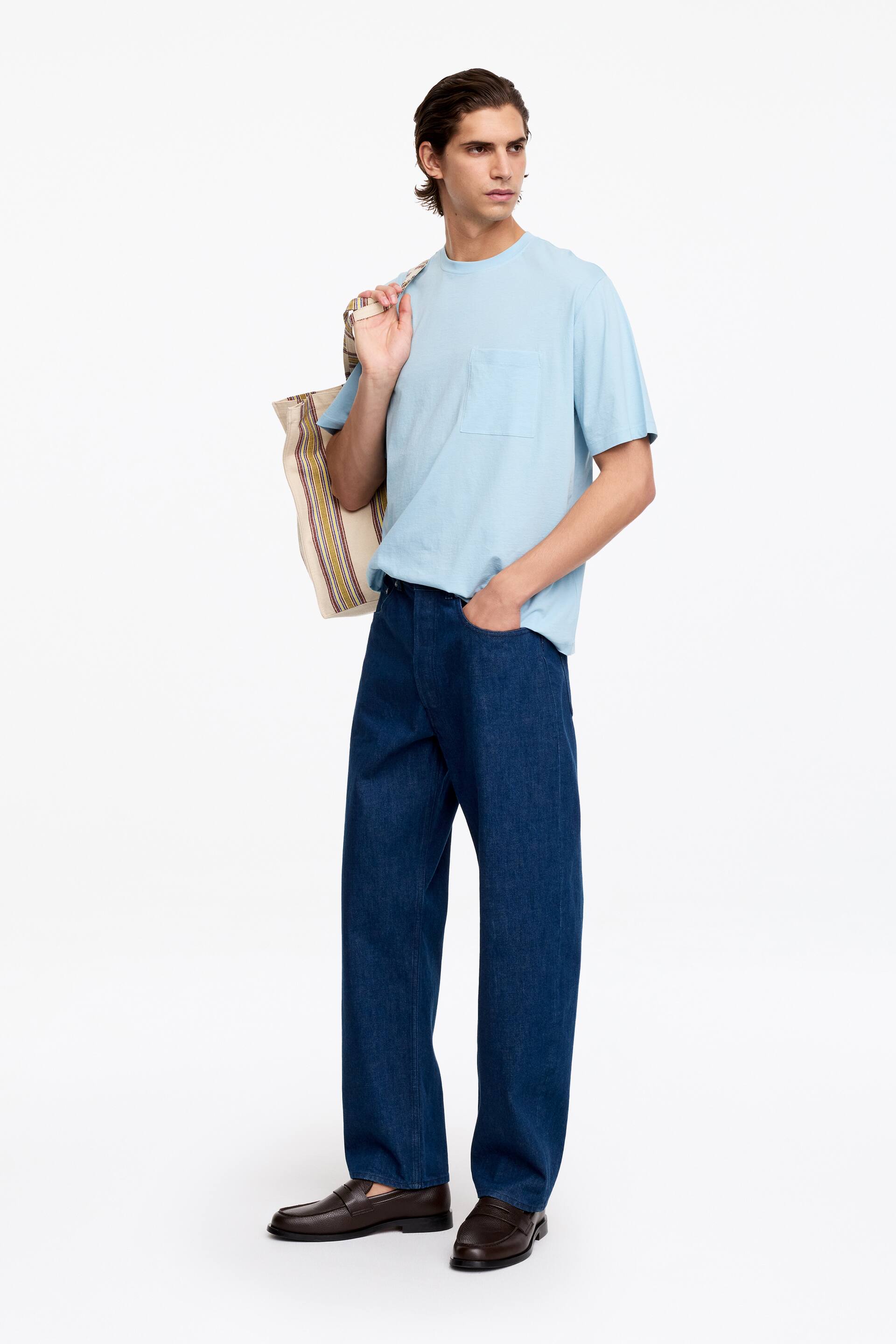 Größeres Bild ansehen: Ein locker sitzendes, hellblaues Kurzarm-T-Shirt mit Rundhalsausschnitt, Rippbündchen und einer einzelnen Brusttasche wird vom Model getragen.