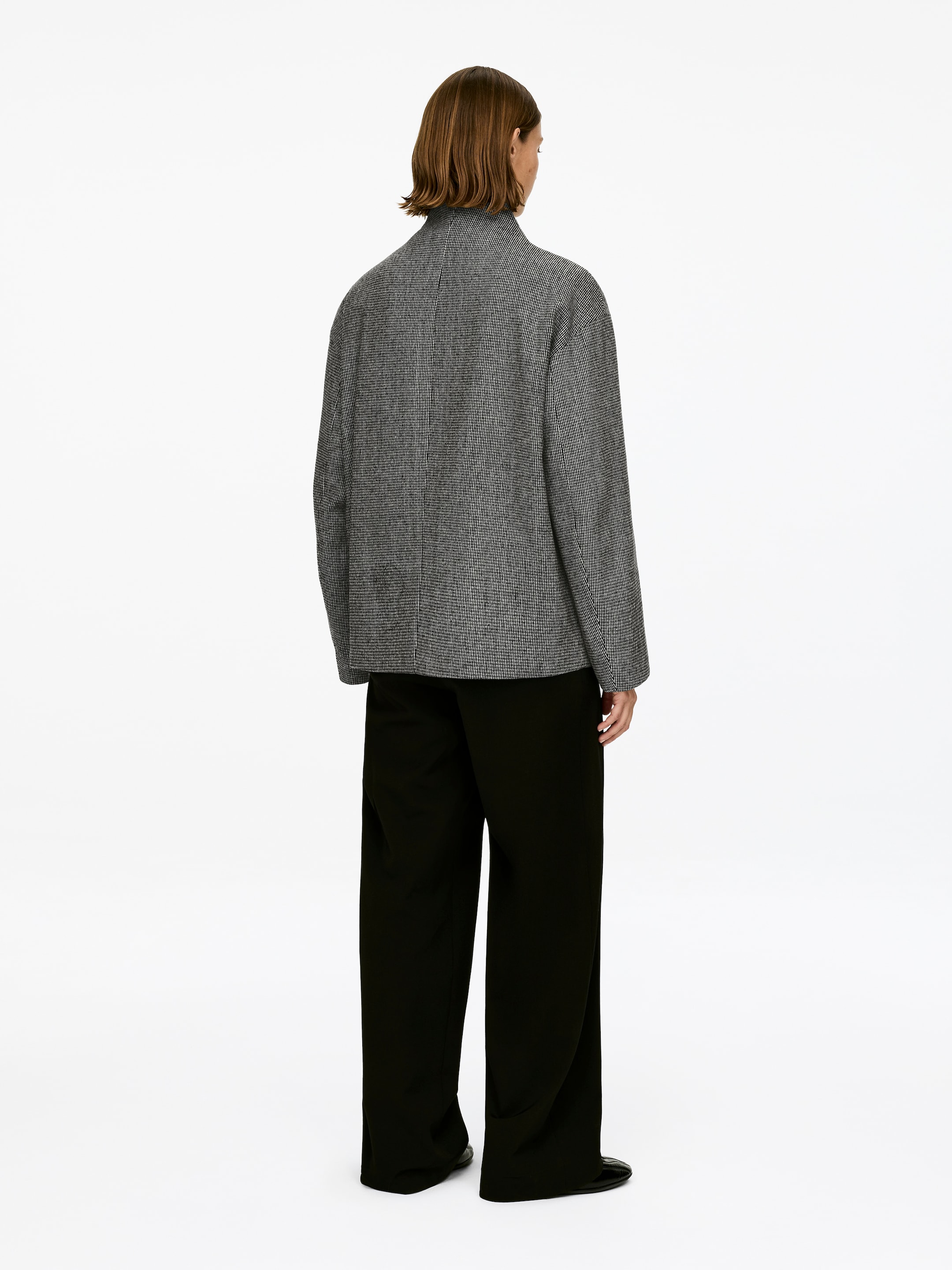 Grösseres Bild ansehen: Eine graue Jacke mit Textur, geschnitten in einer übergroßen und abgerundeten Silhouette, wird vom Model getragen. Sie hat einen hohen Kragen an der Rückseite.